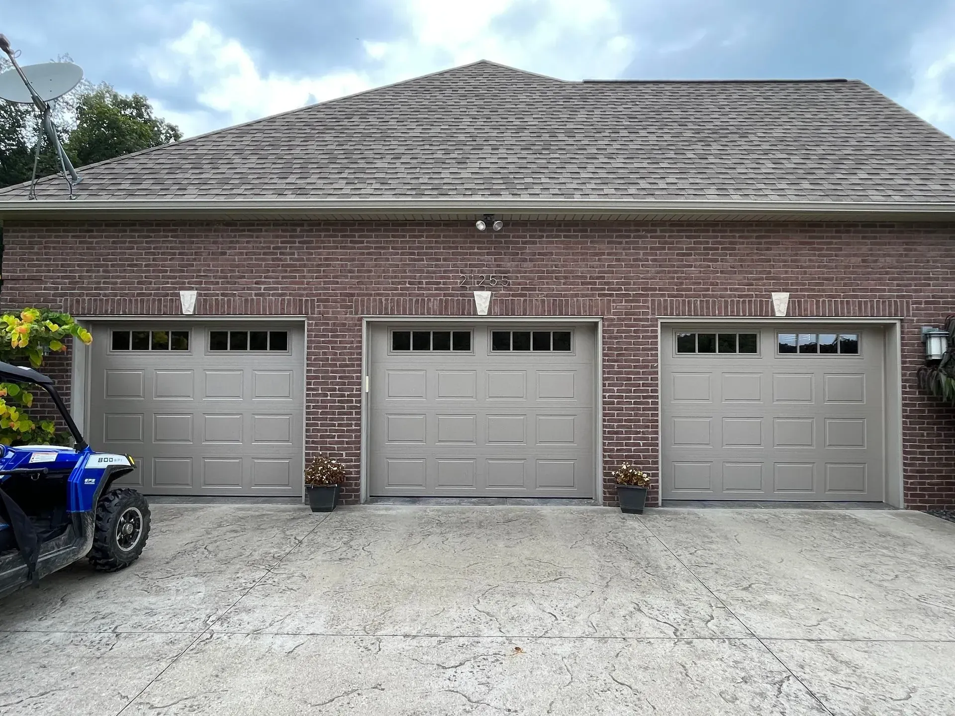Three-car brick garage with gray doors and a blue ATV on the left side