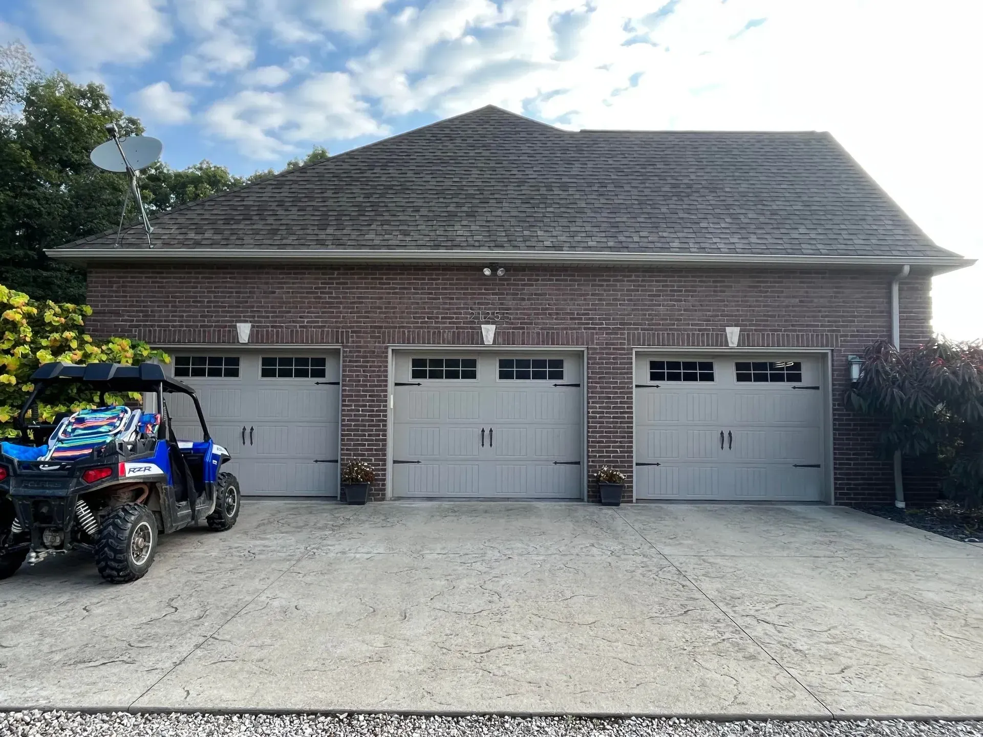 Brick house with three garage doors and a parked blue ATV in the driveway