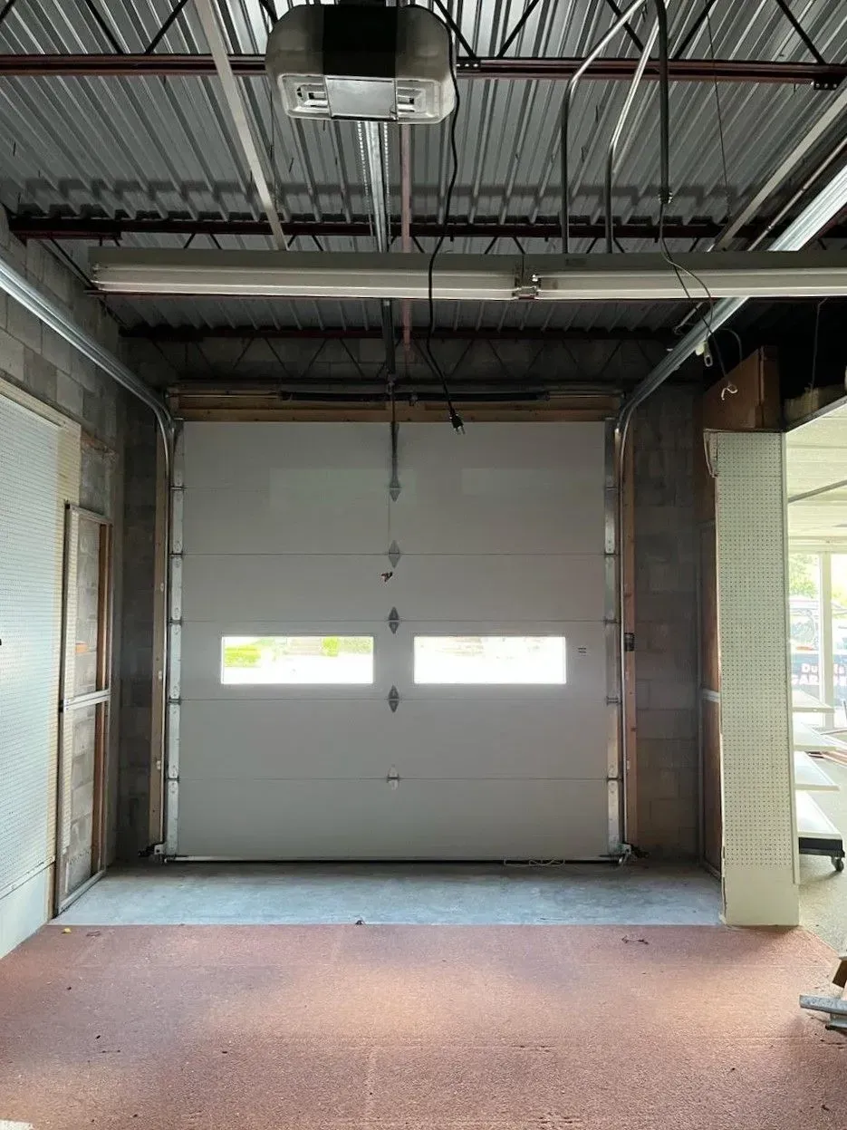 Empty industrial garage bay with closed gray overhead door and exposed ceiling pipes