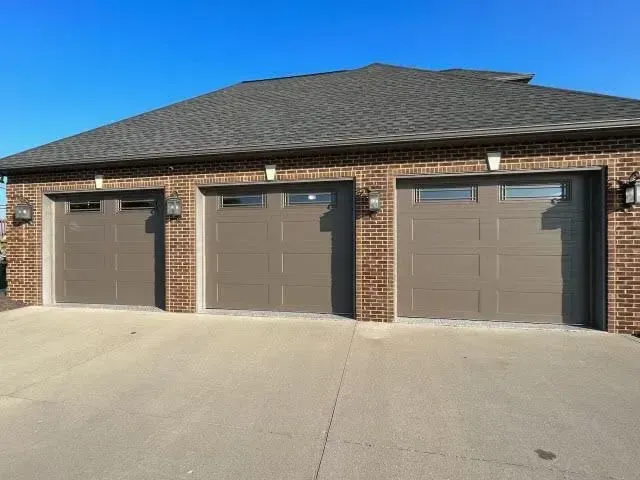 Three closed brown garage doors on a brick house with a concrete driveway