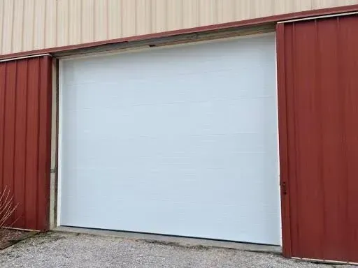 White roll-up garage door on a red metal building exterior