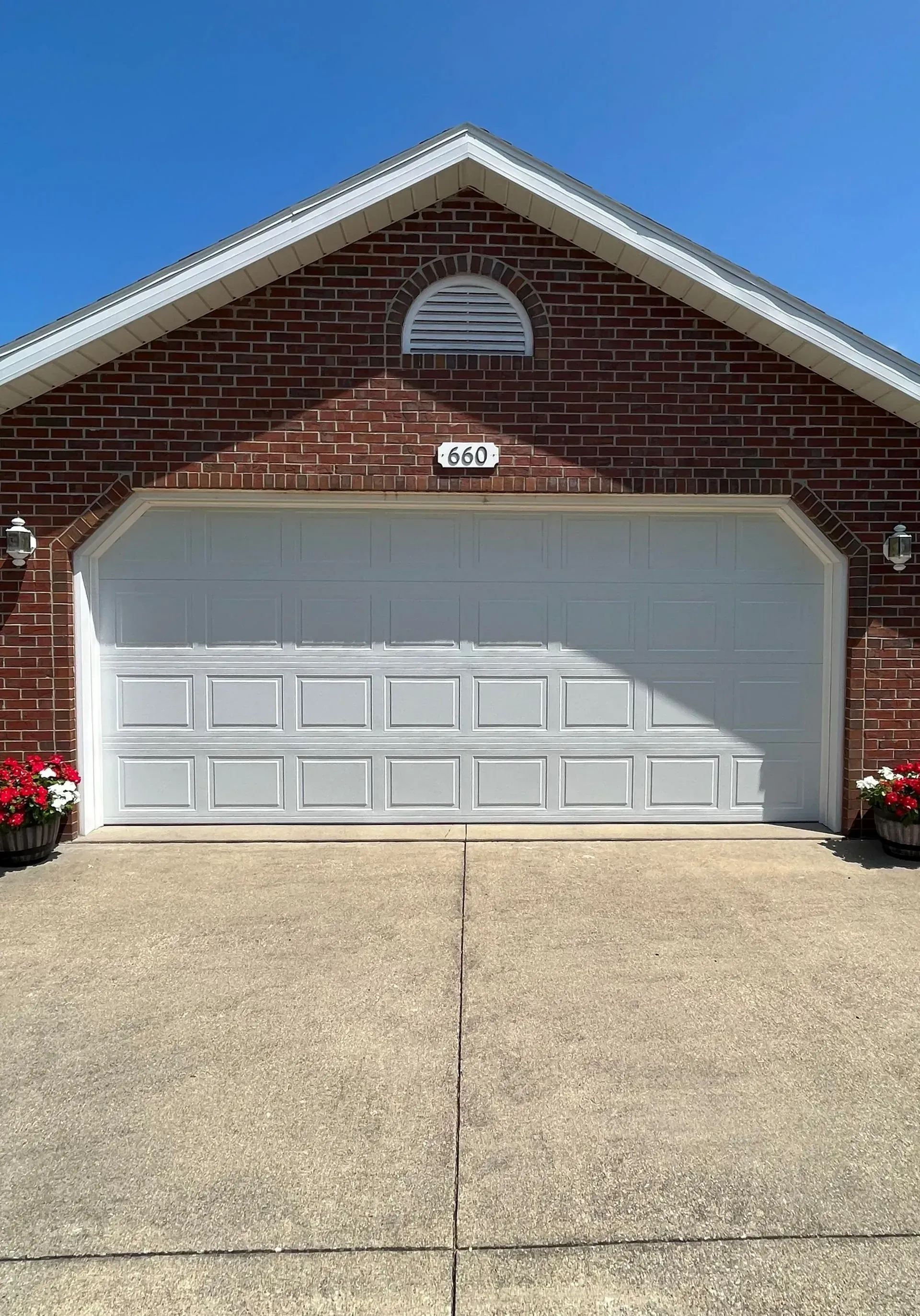 Brick house with a white garage door and concrete driveway under a blue sky