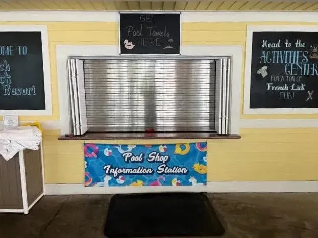 Poolside towel station with a service window, colorful sign, and black mat