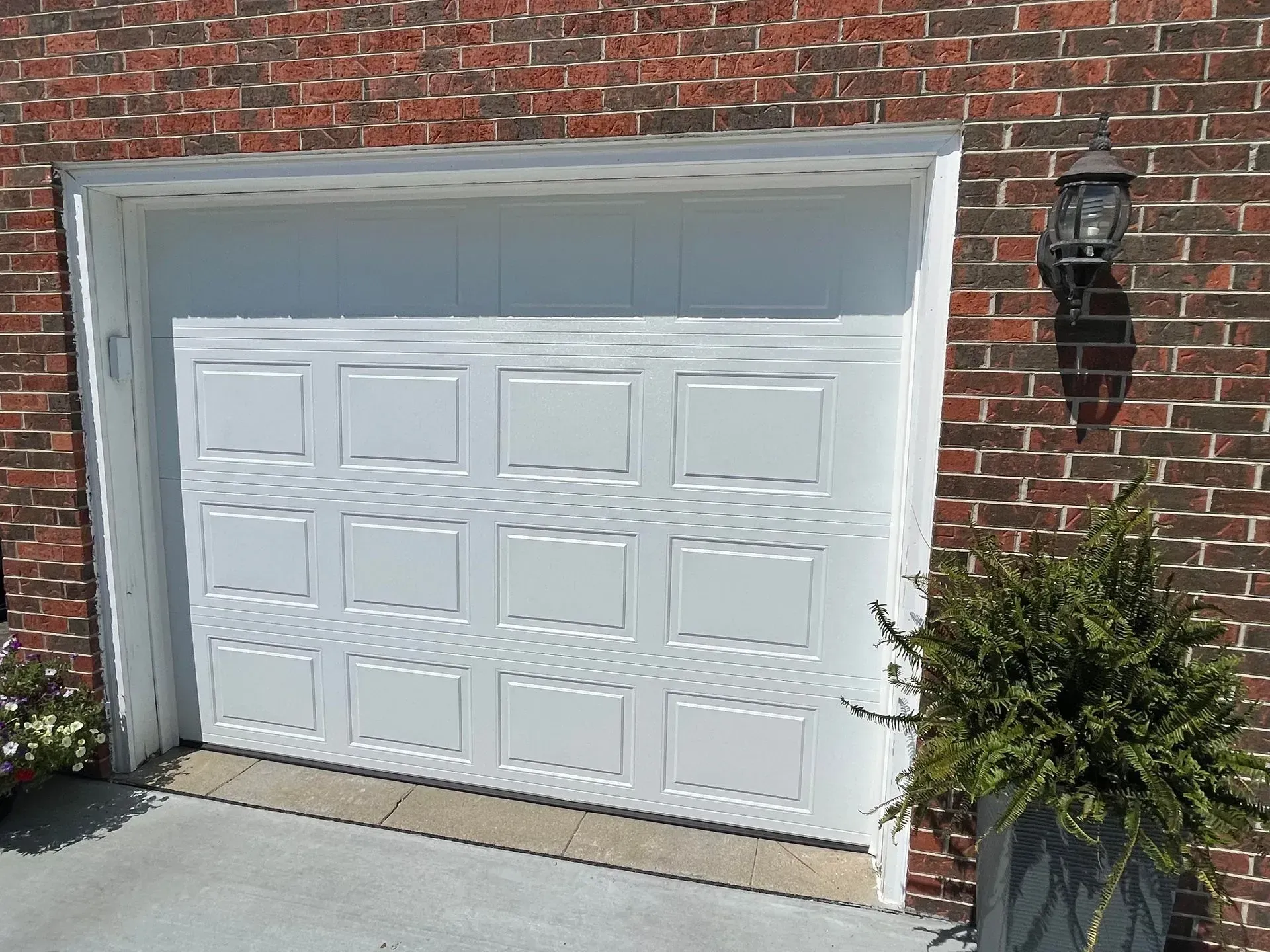 White garage door on a red brick house with a wall lantern and potted plant beside it