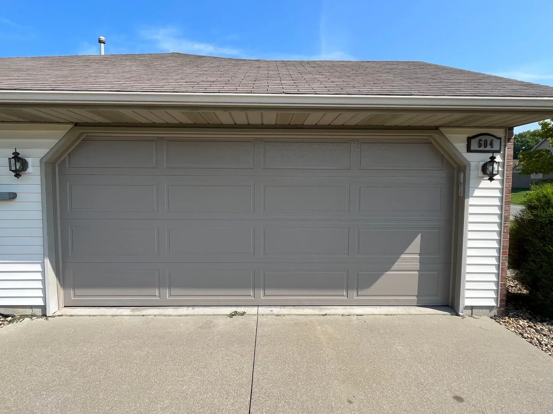 Two-car garage with closed gray doors under a shingled roof, viewed from the driveway