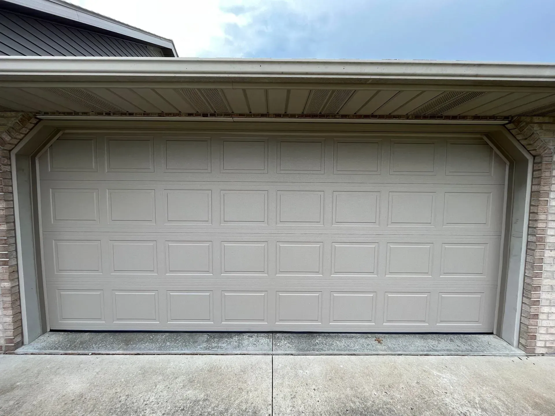 Closed white garage door with rectangular paneling under a house roof overhang