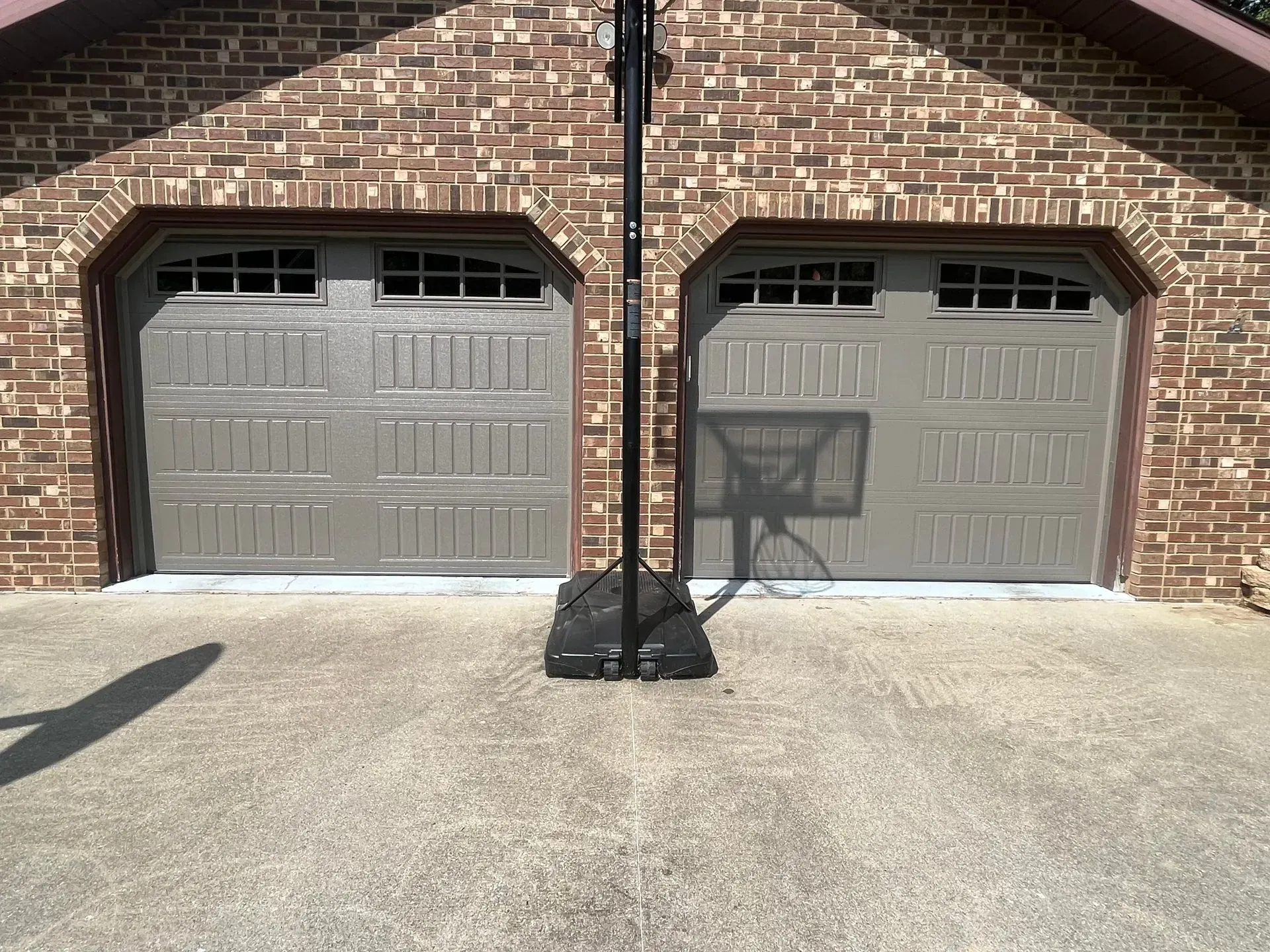Two gray garage doors in a brick house facade, with a black post centered on the driveway.