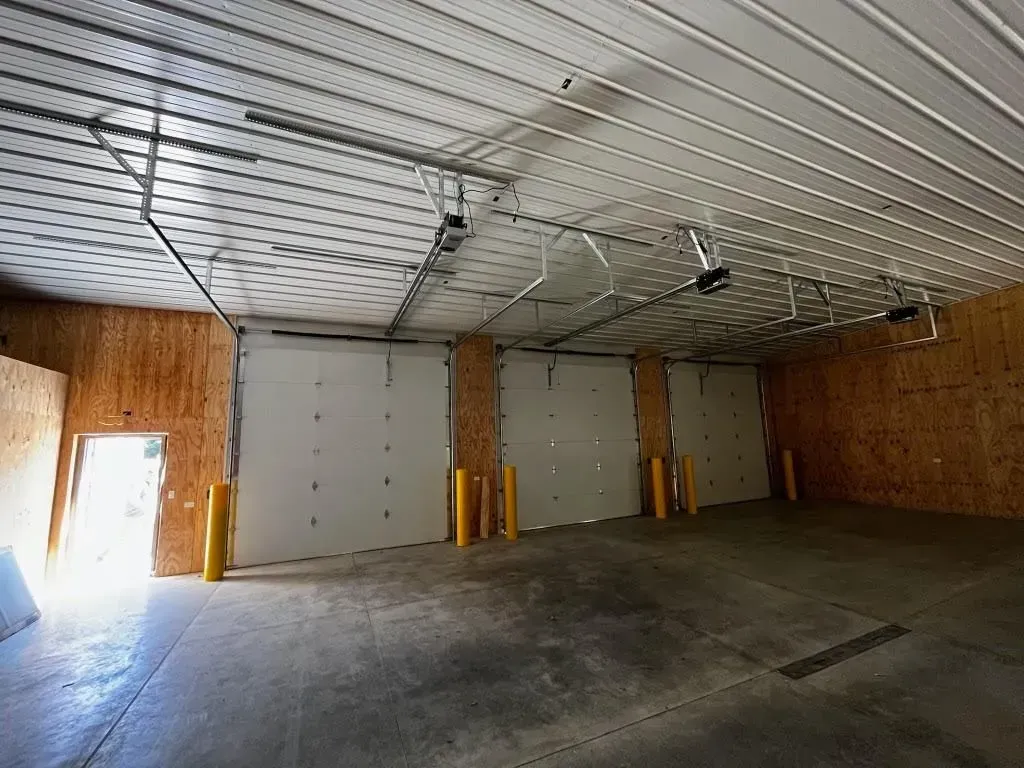 Empty warehouse interior with concrete floor, roll-up doors, and bright light from an open side door