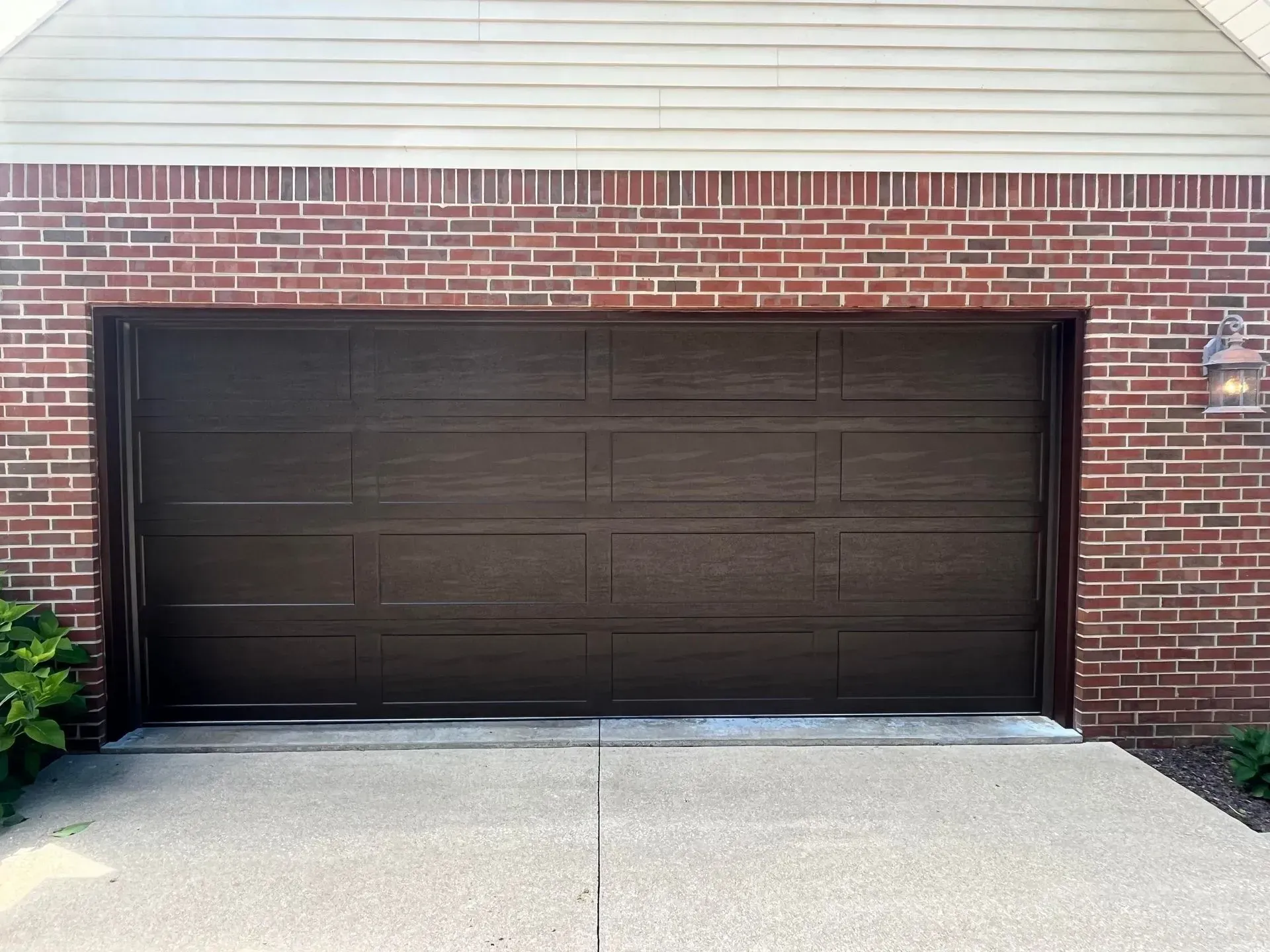 Dark brown garage door set in a red brick house exterior above a concrete driveway