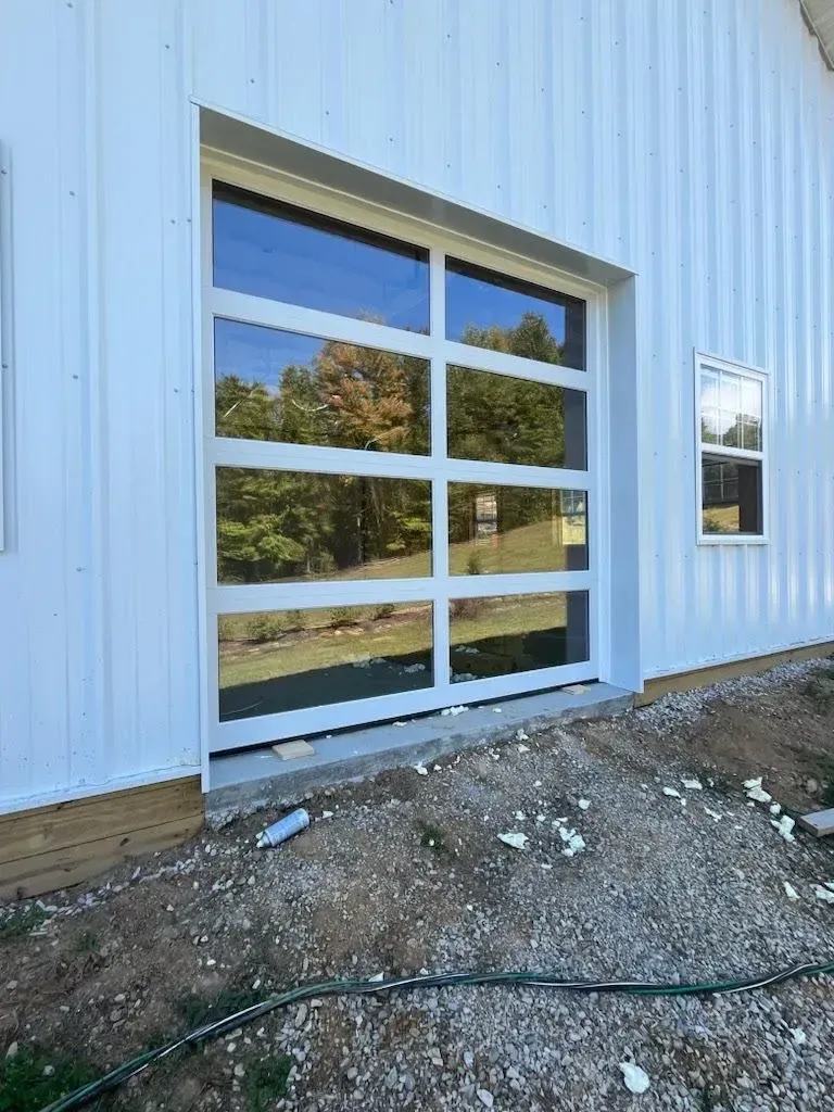 Large glass garage door on a white metal building, with gravel and a hose in the foreground.