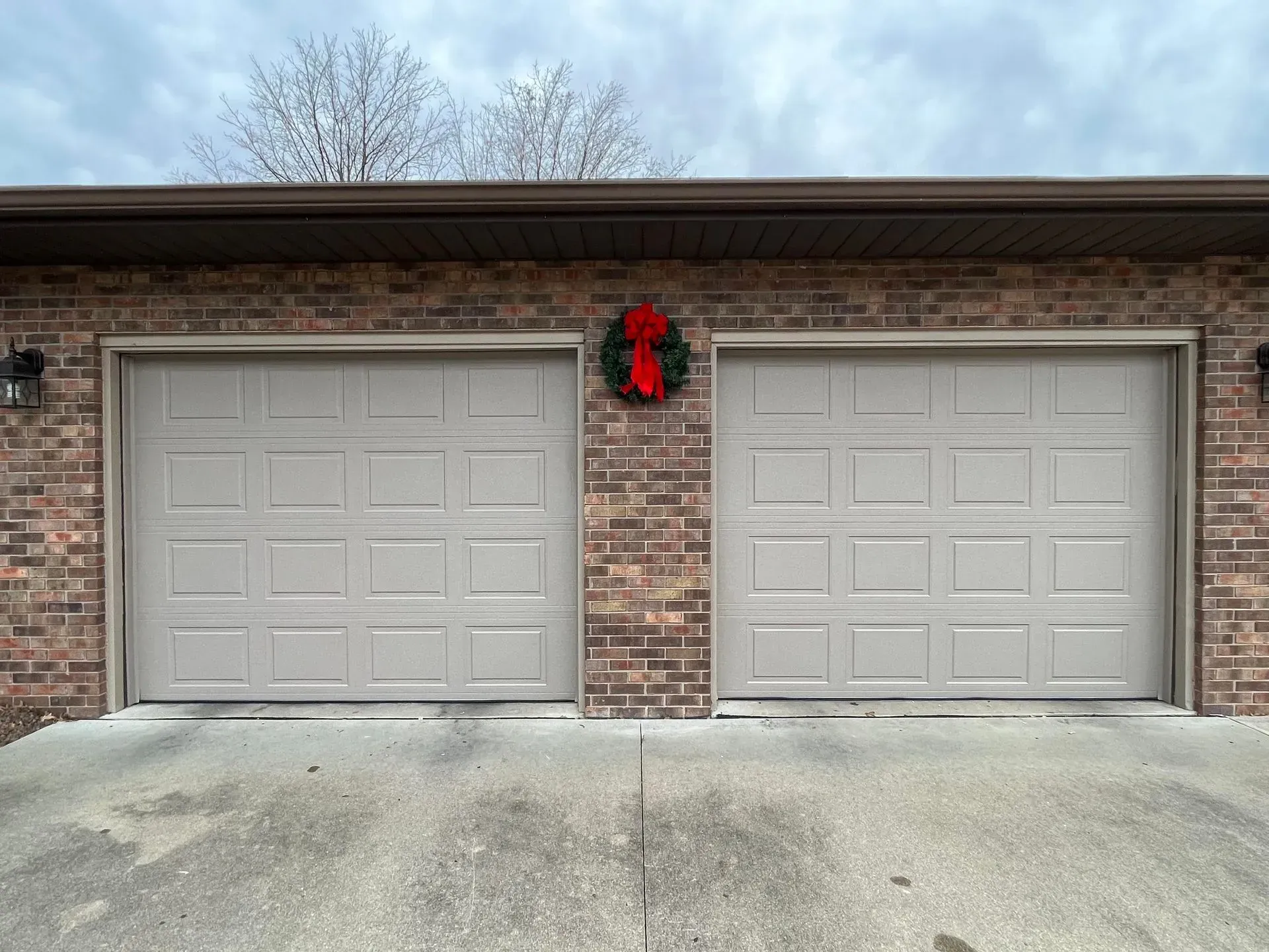 Brick house front with two beige garage doors and a red wreath between them