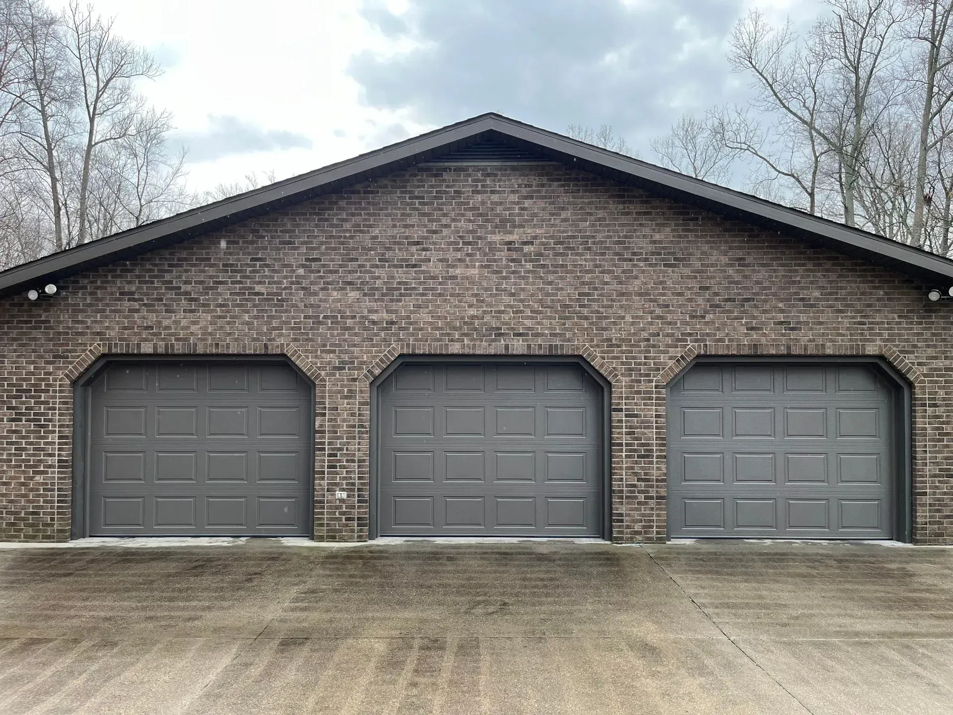 Brick house with three gray garage doors under a cloudy sky