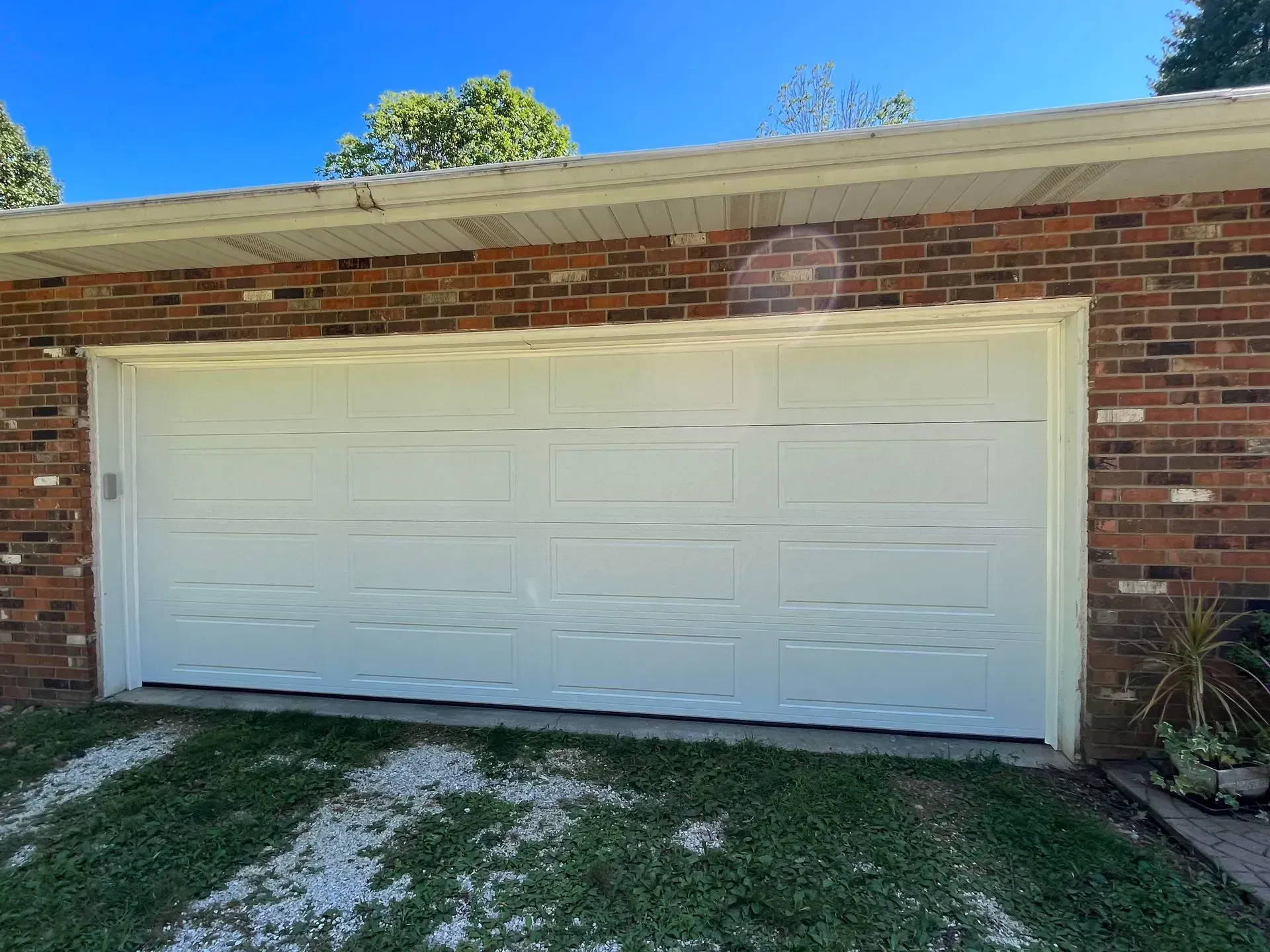 White double garage door on a brick house with a small grass driveway and blue sky above