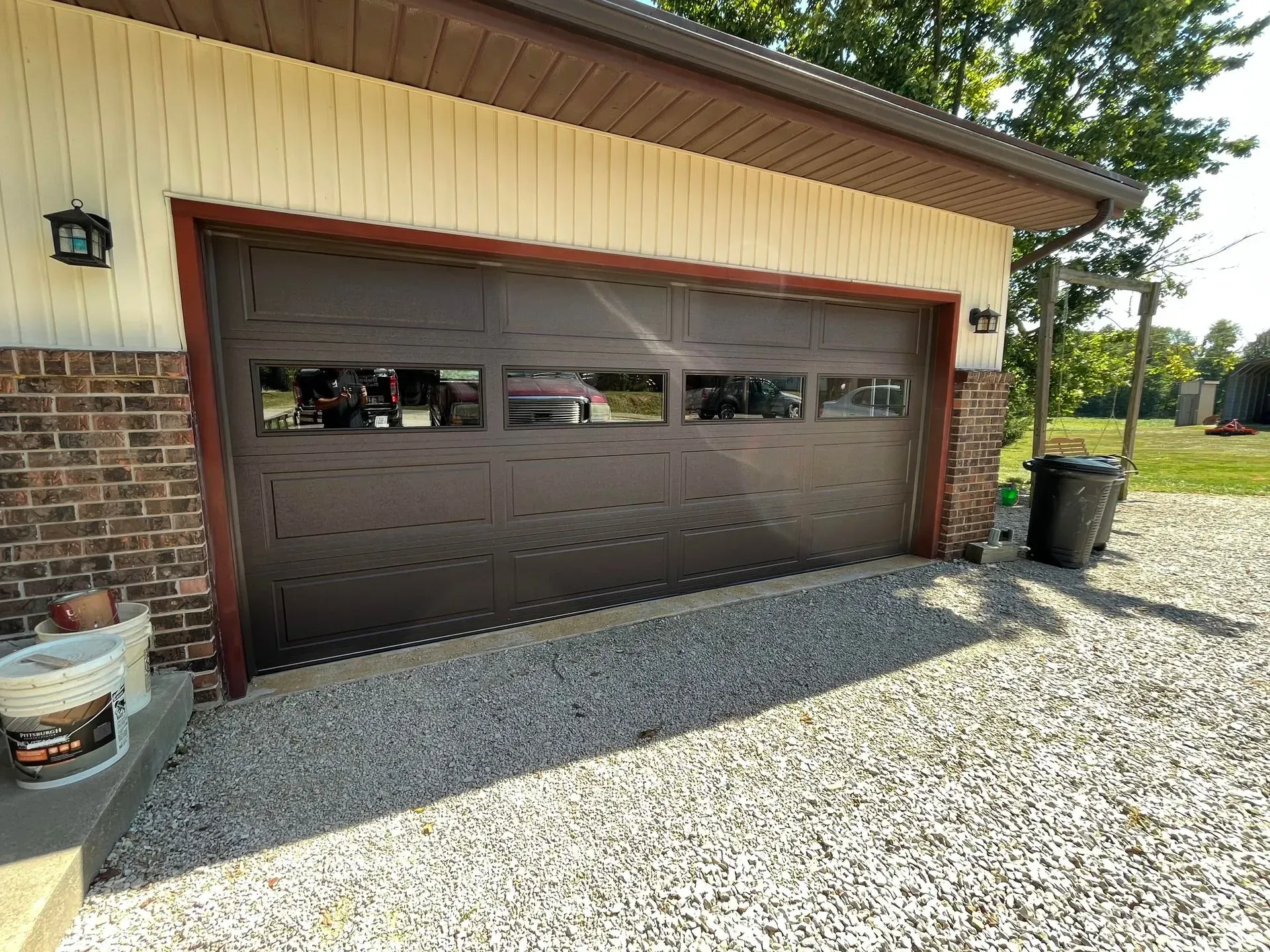 Brown garage door on a tan house with gravel driveway and brick trim