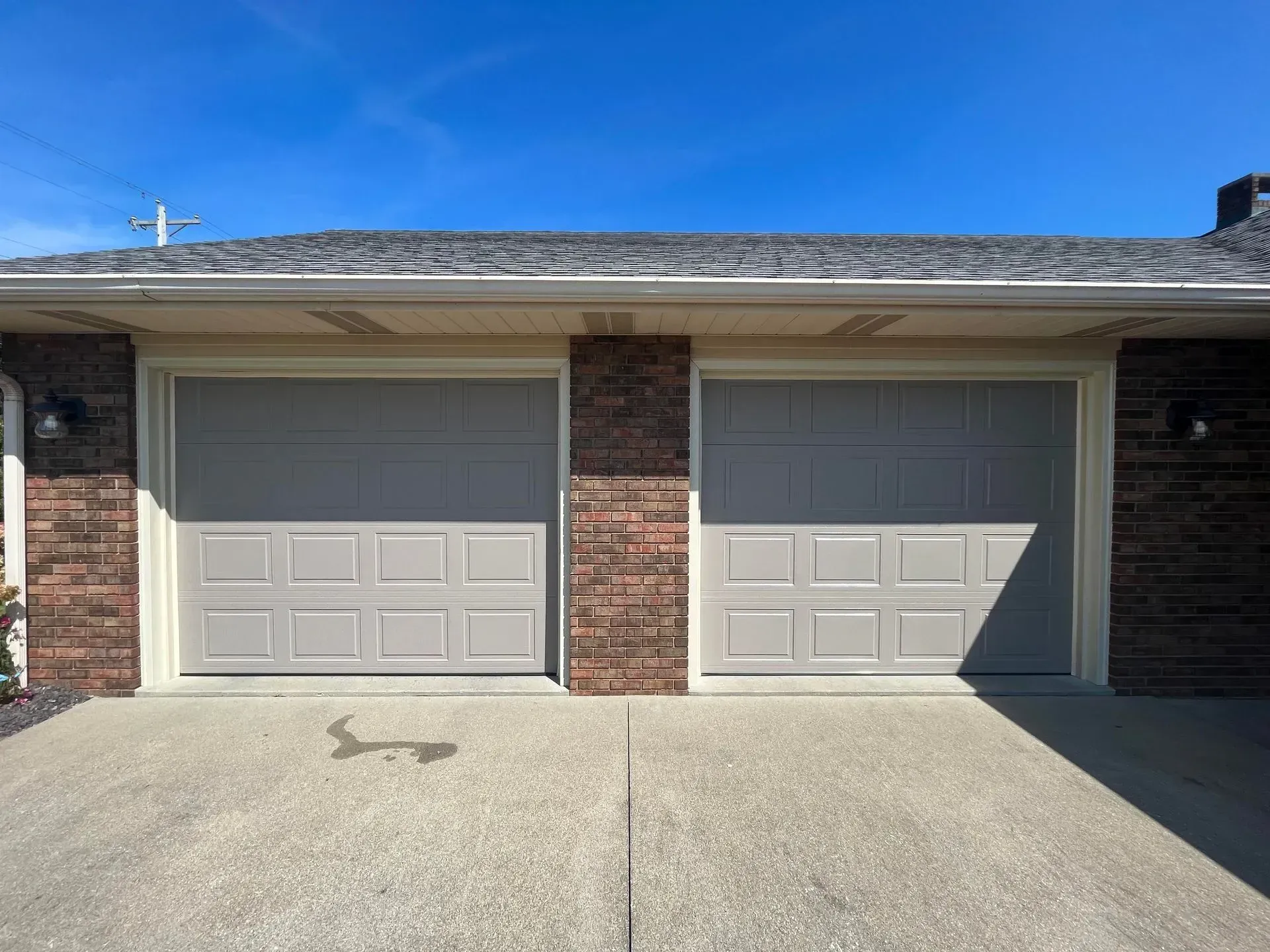 Two-car garage with closed beige doors on a brick townhouse, concrete driveway in front
