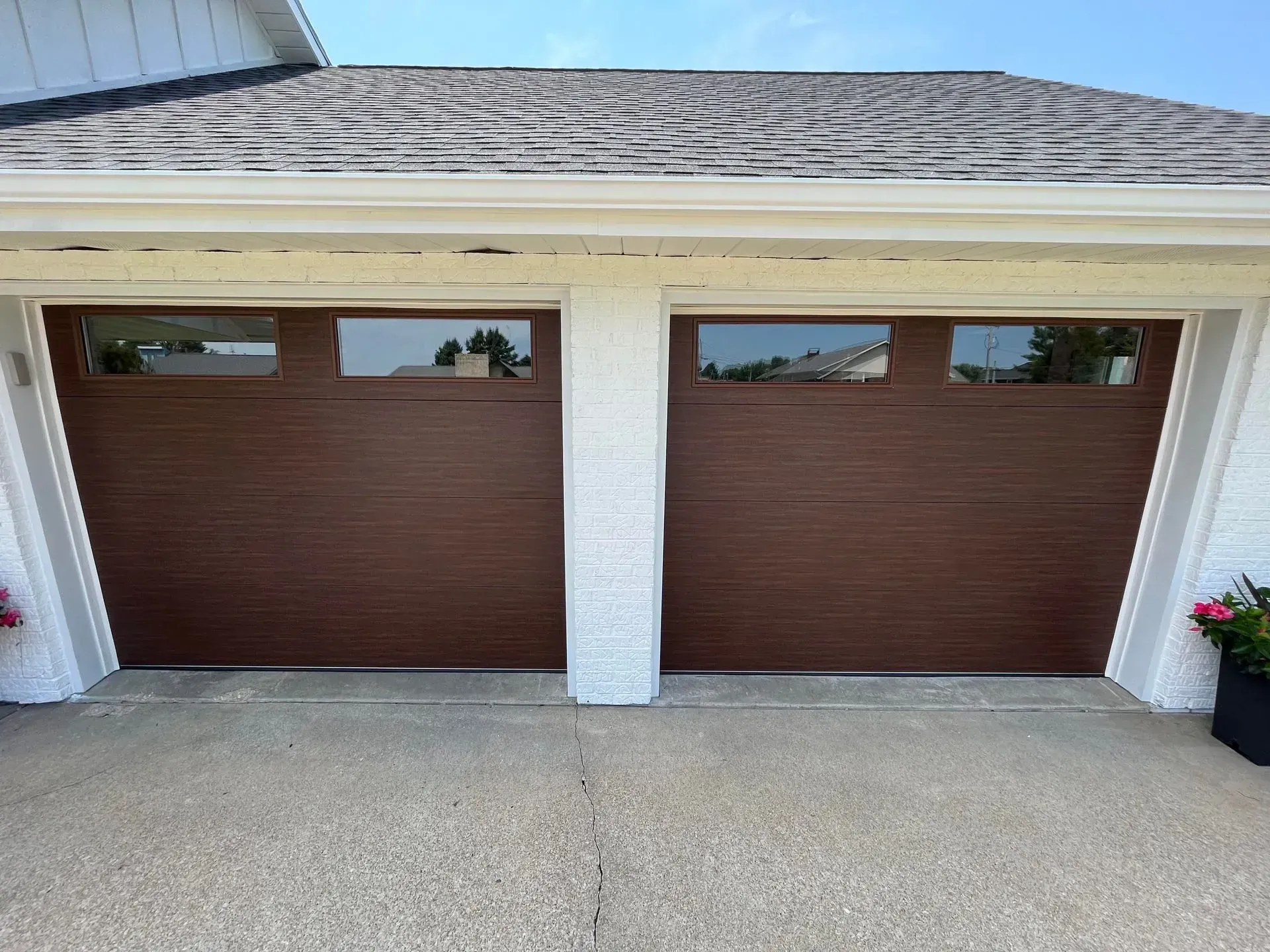 Two brown garage doors on a house with white trim and a concrete driveway