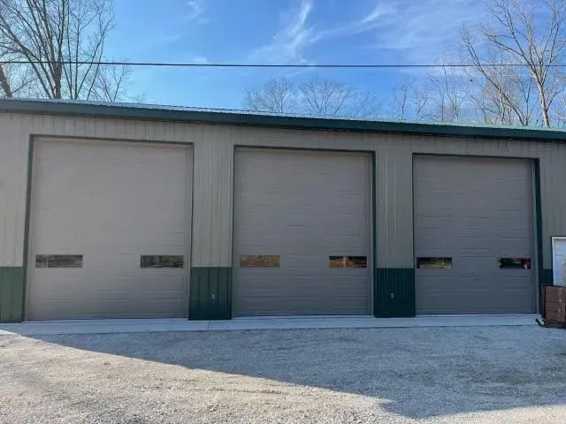 Three beige garage doors on a metal building with gravel foreground and blue sky above