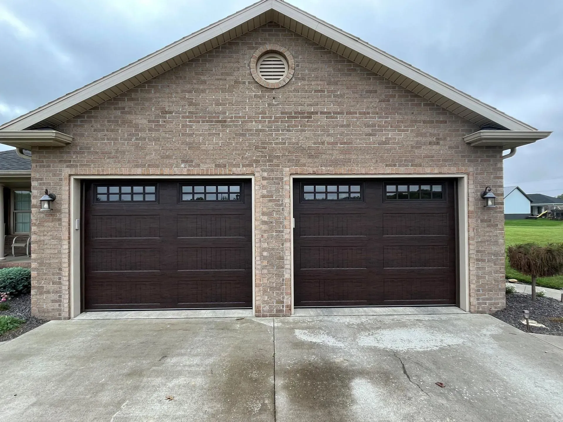 Brick house front with two dark garage doors and a concrete driveway