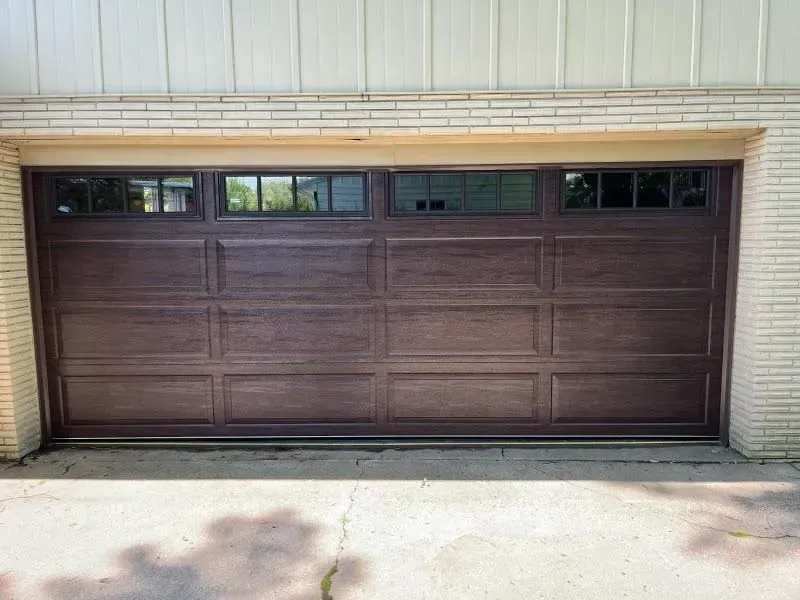 Brown garage door with narrow windows set in a beige exterior wall