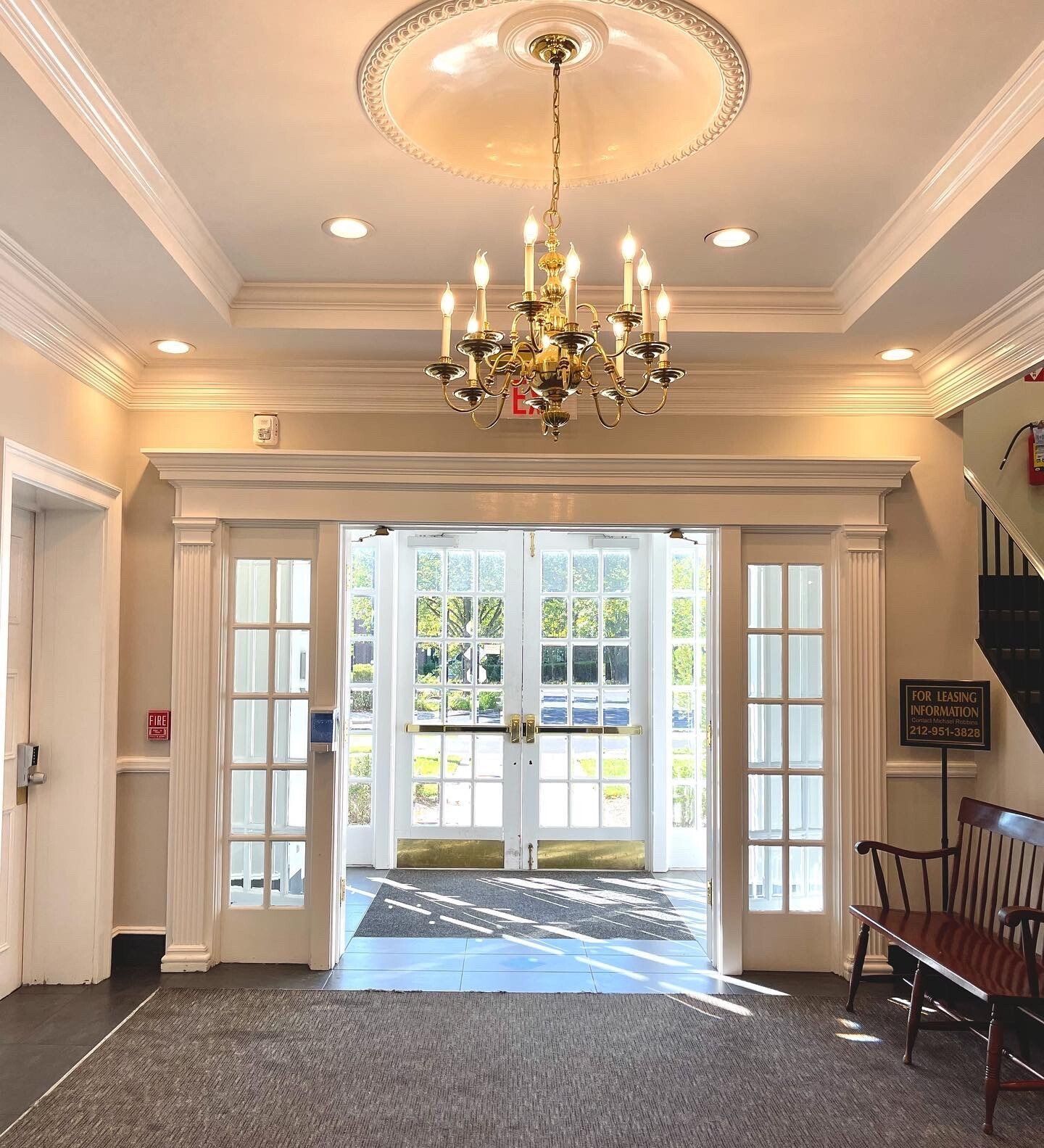 Elegant entrance hall with chandelier, glass doors leading outside, and a bench.