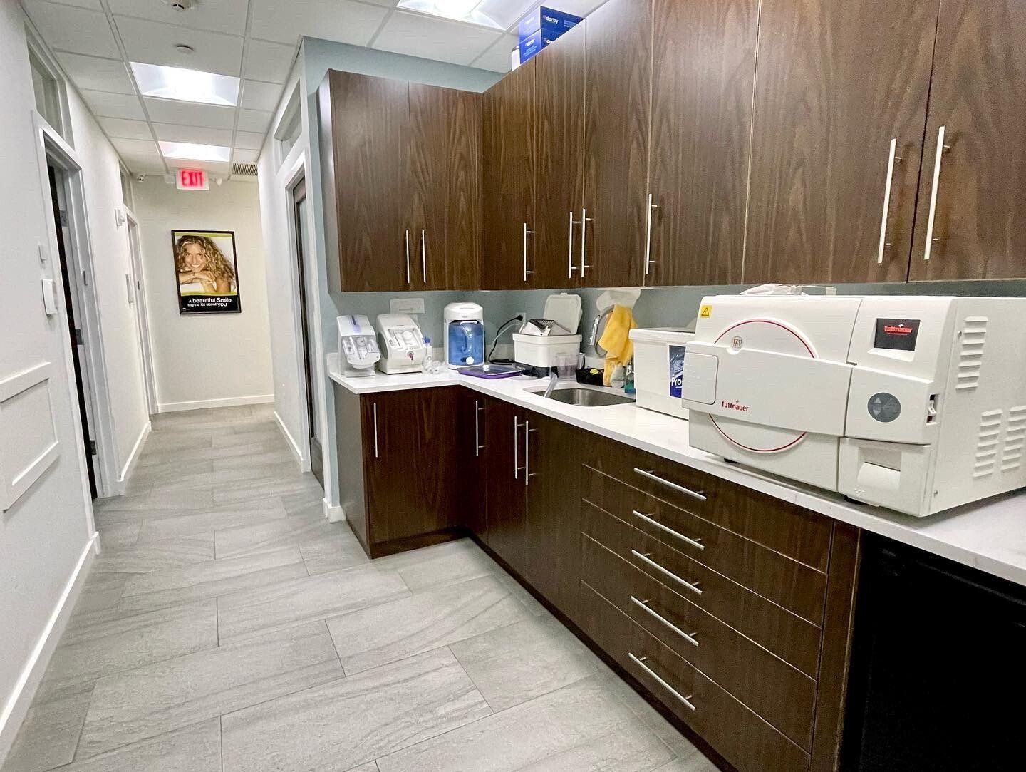 Dental office interior with brown cabinets, autoclave, and a hallway with a poster.
