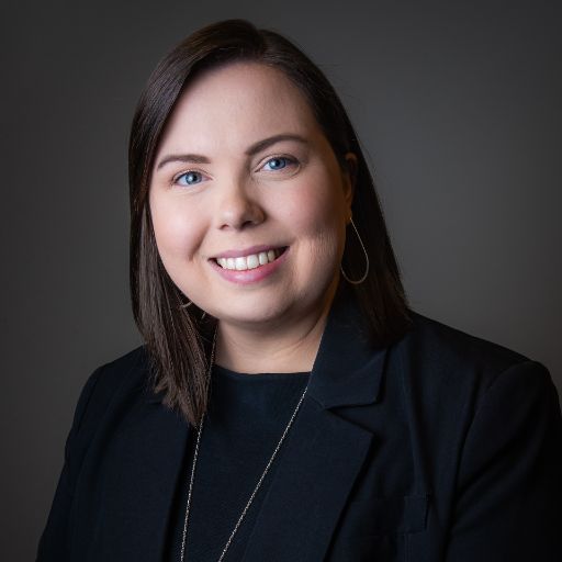 Professional headshot of a smiling person in a black blazer against a dark background