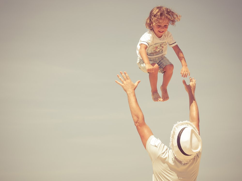 father tossing son in the air on a sunny day