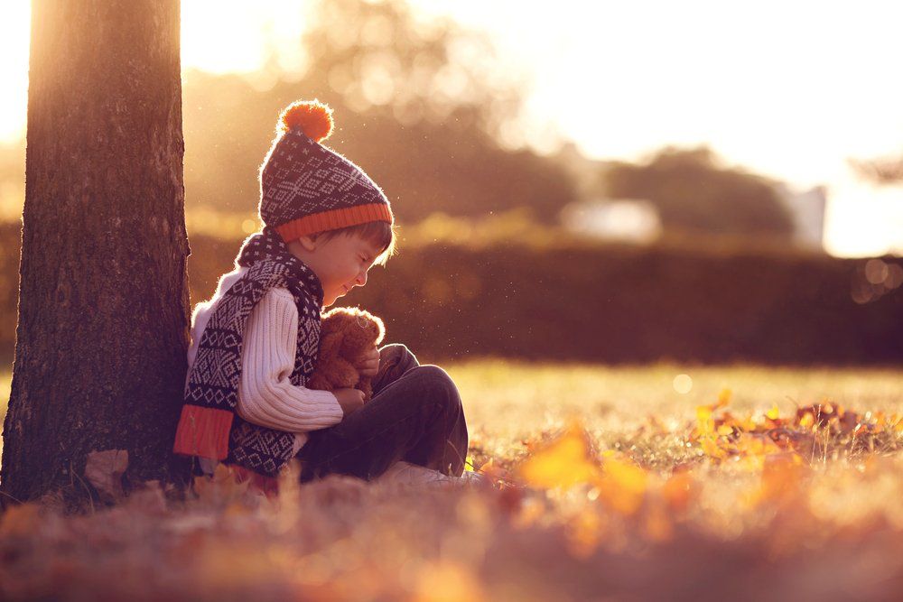 Child holding a stuffed bear outside under a tree