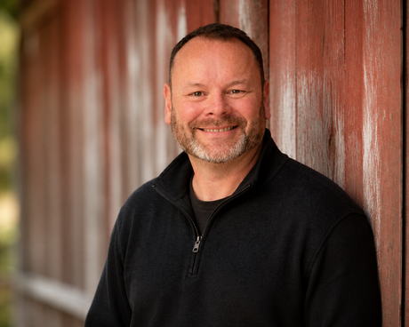 A man wearing a blue shirt and a black vest is smiling for the camera.