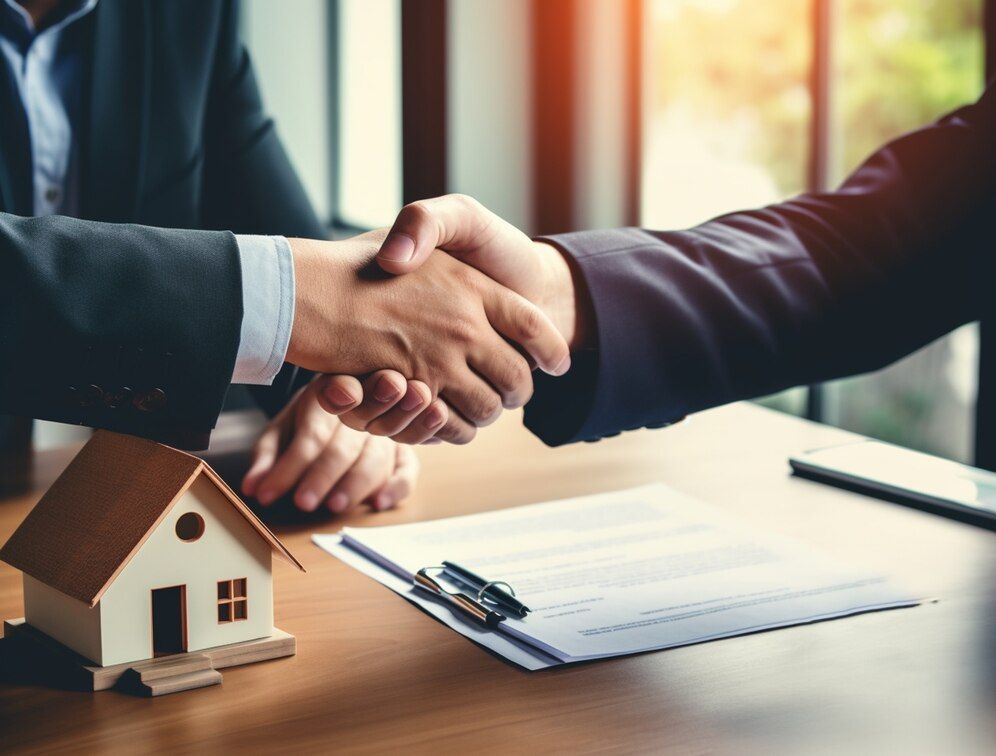 Two men are shaking hands over a table with a model house on it.