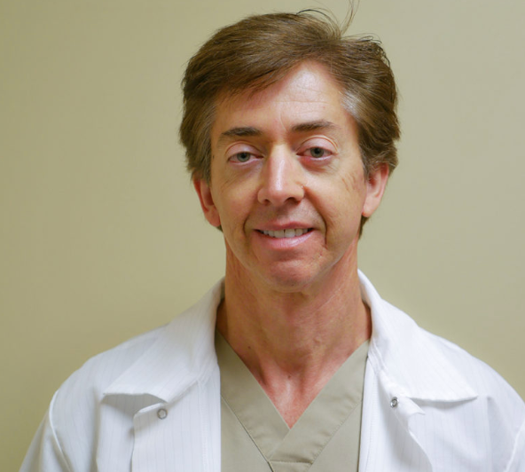 A man wearing a white lab coat and scrubs smiles for the camera