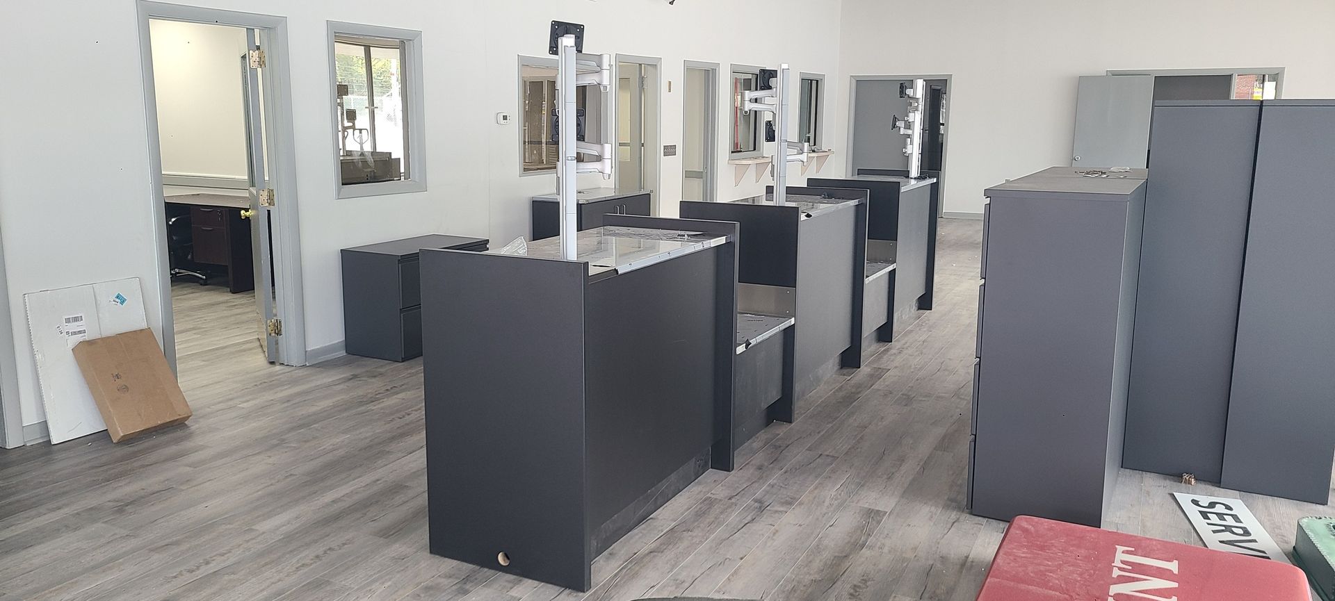Empty office space with gray cabinets, black desks, and mirrors on wood-look flooring