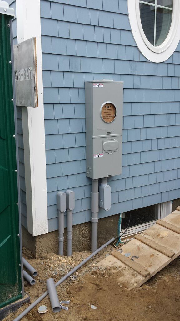 Gray utility meter box and pipes mounted on a blue shingled house exterior near a window.