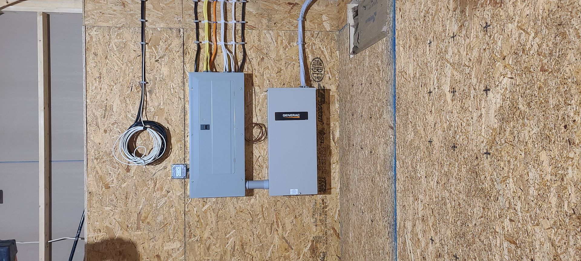 Wall-mounted electrical panels with conduit and a coiled cable on a textured exterior wall.