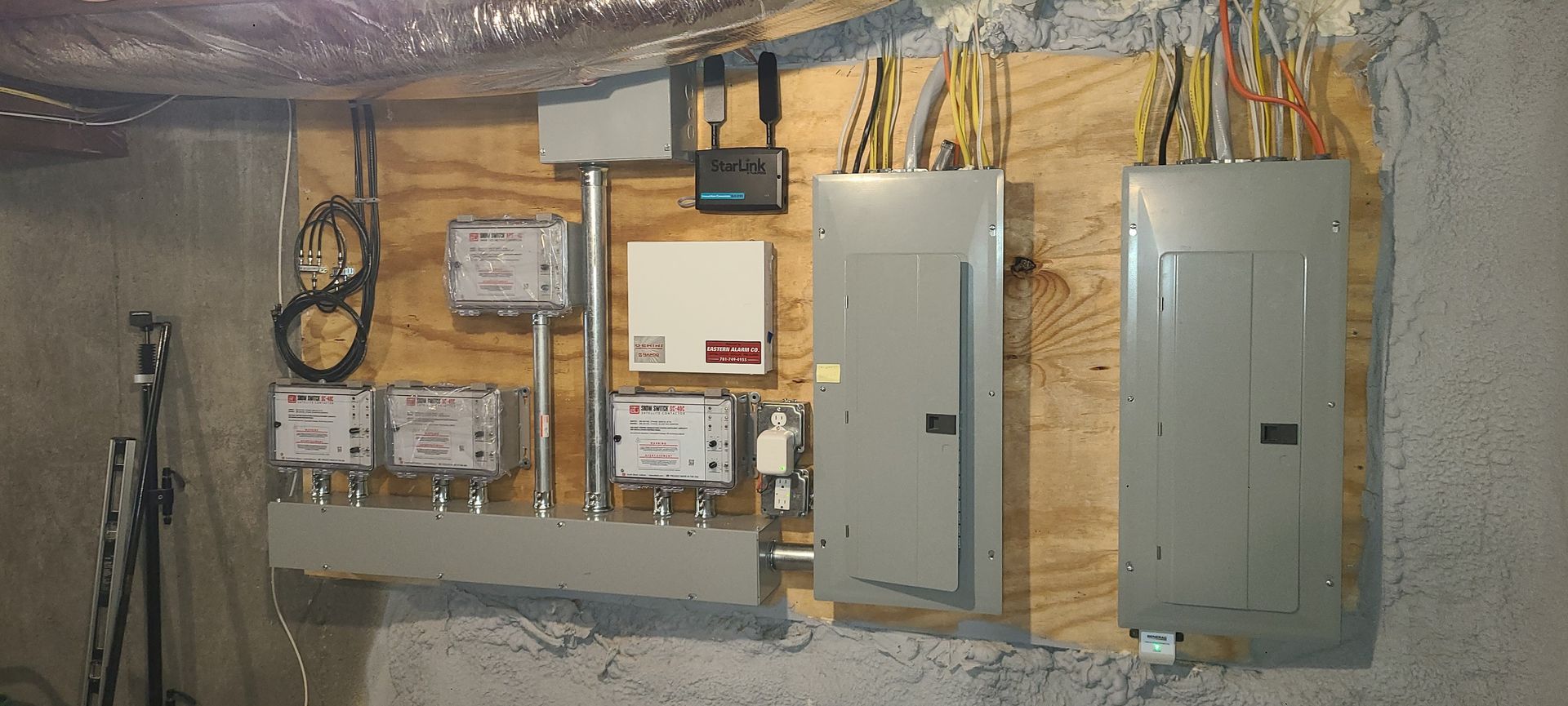 Basement utility wall with electrical panels, meters, and exposed insulation and wiring.
