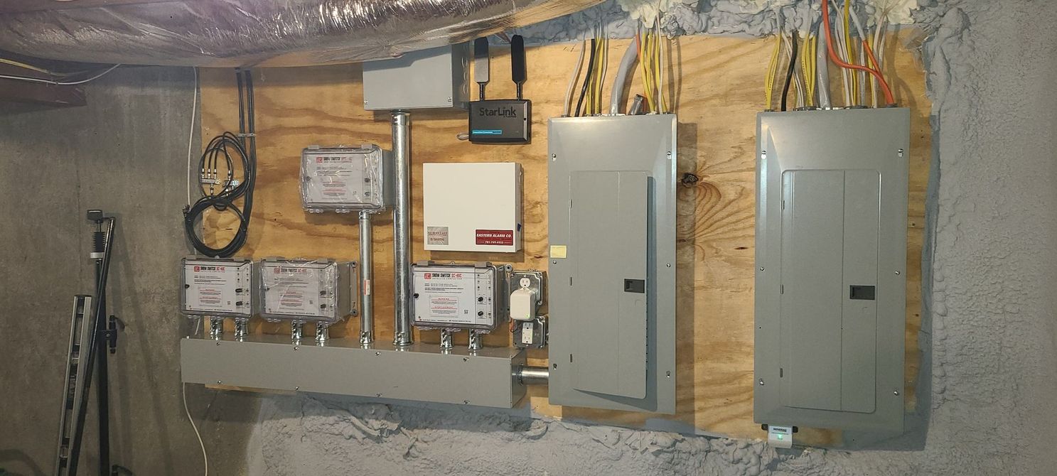 Basement utility wall with electrical panels, meters, and exposed insulation and wiring.