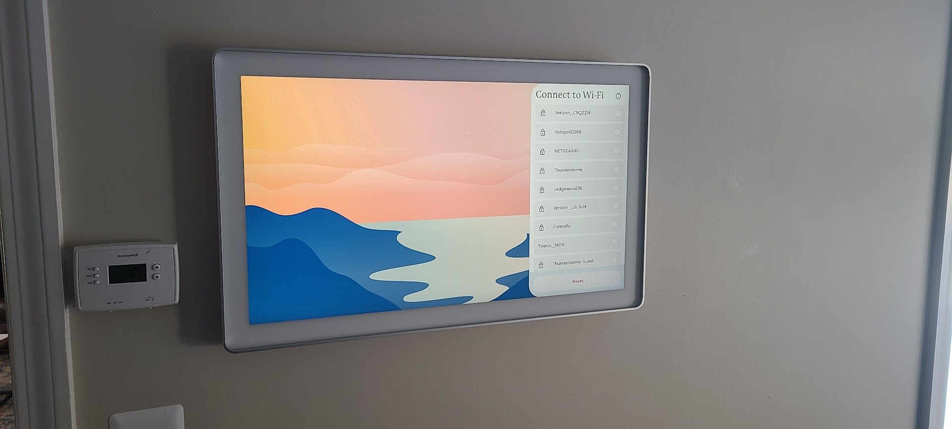 Wall-mounted touchscreen displaying a scenic sunset wallpaper in a gray room