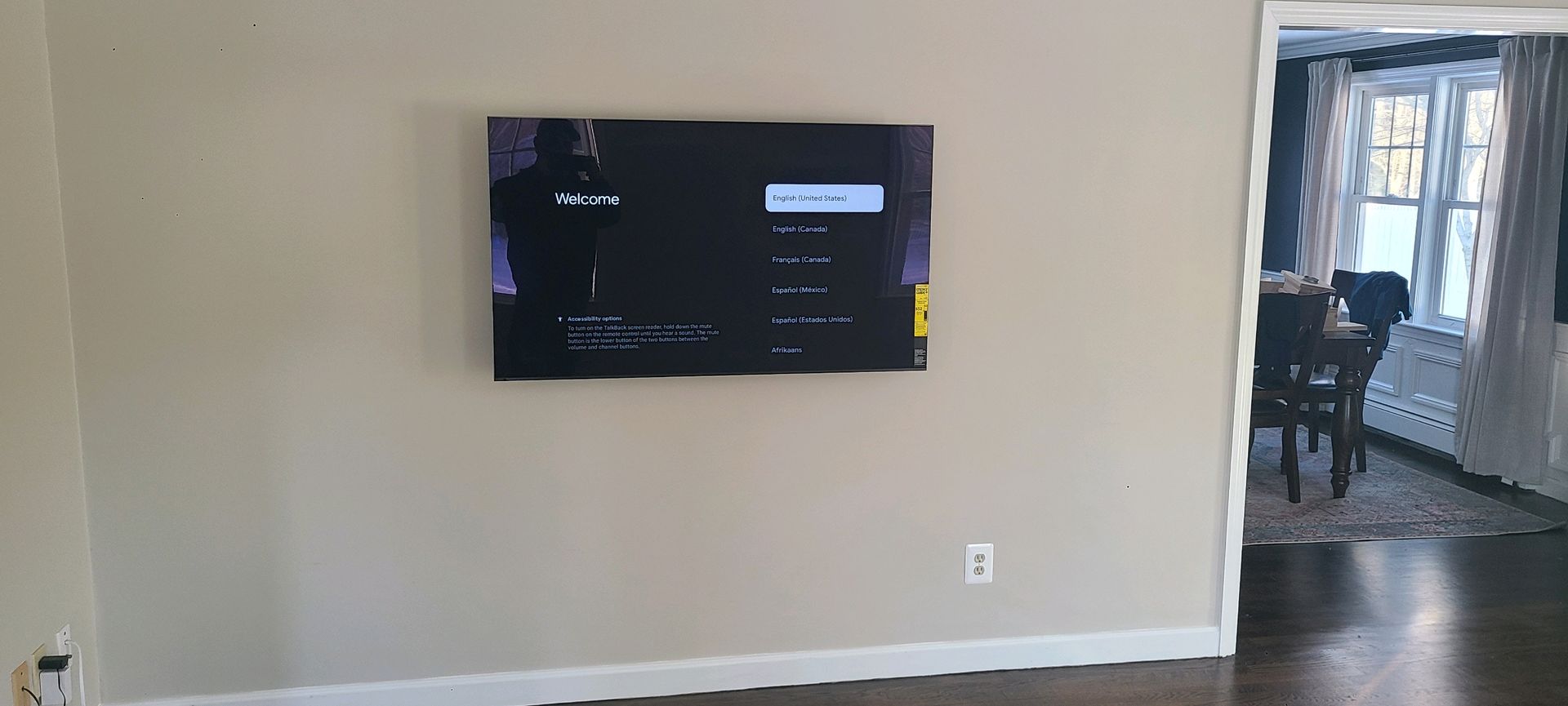 Wall-mounted TV in a beige living room, with a window and doorway on the right.