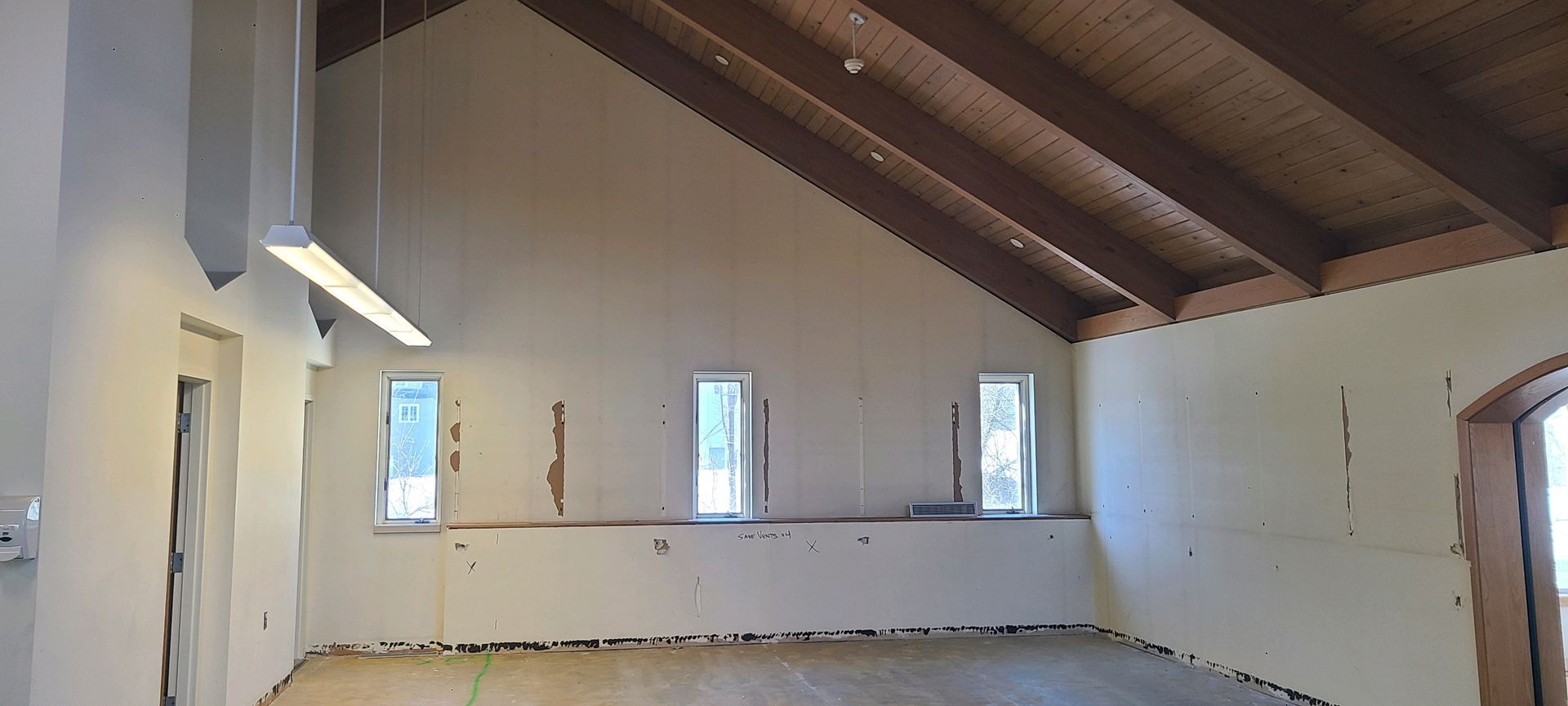 Empty attic room with white walls, exposed wooden beams, and small windows along one side