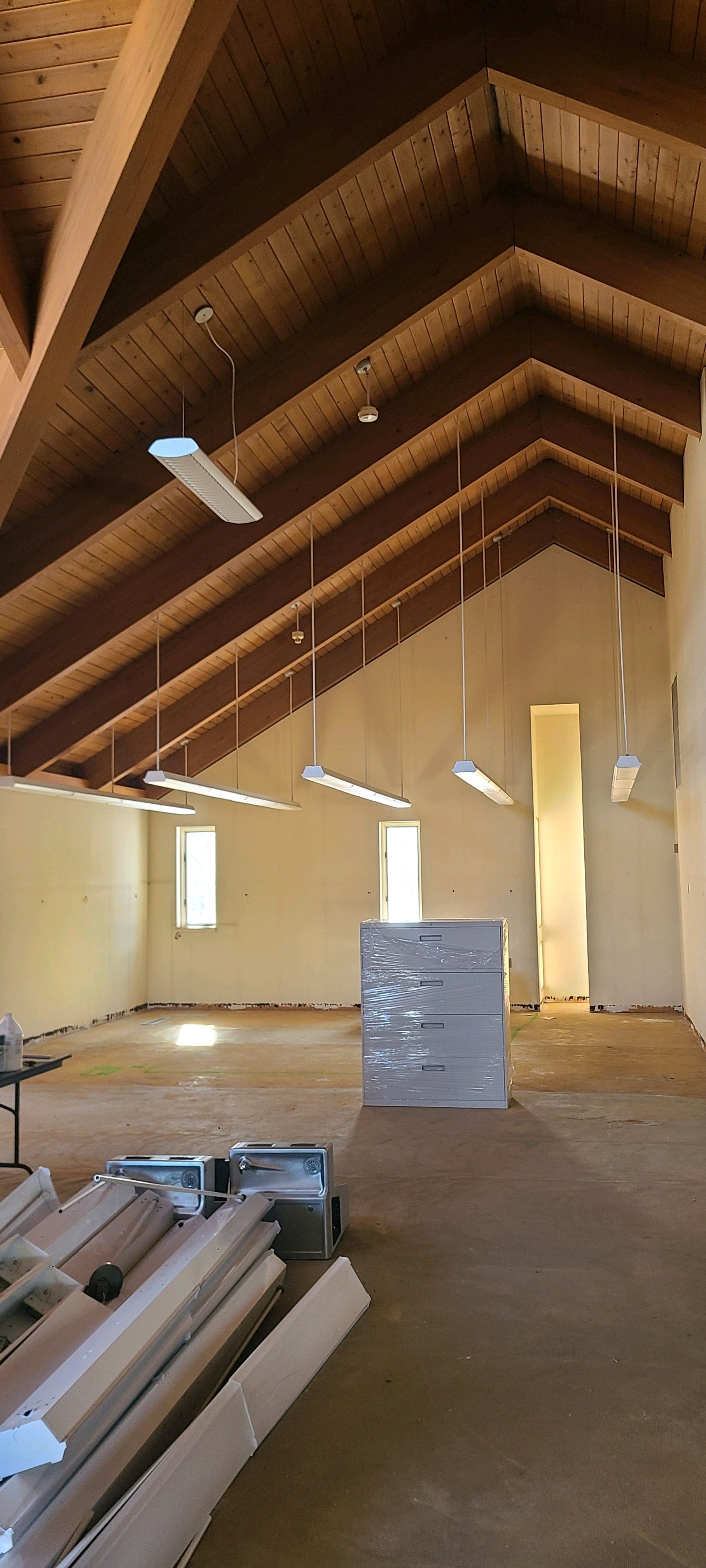 Large unfinished attic with exposed wooden beams, stacked lumber, and hanging light fixtures.