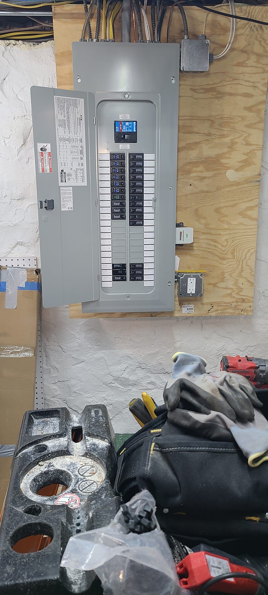 Breaker panel mounted on plywood wall above construction tools and debris