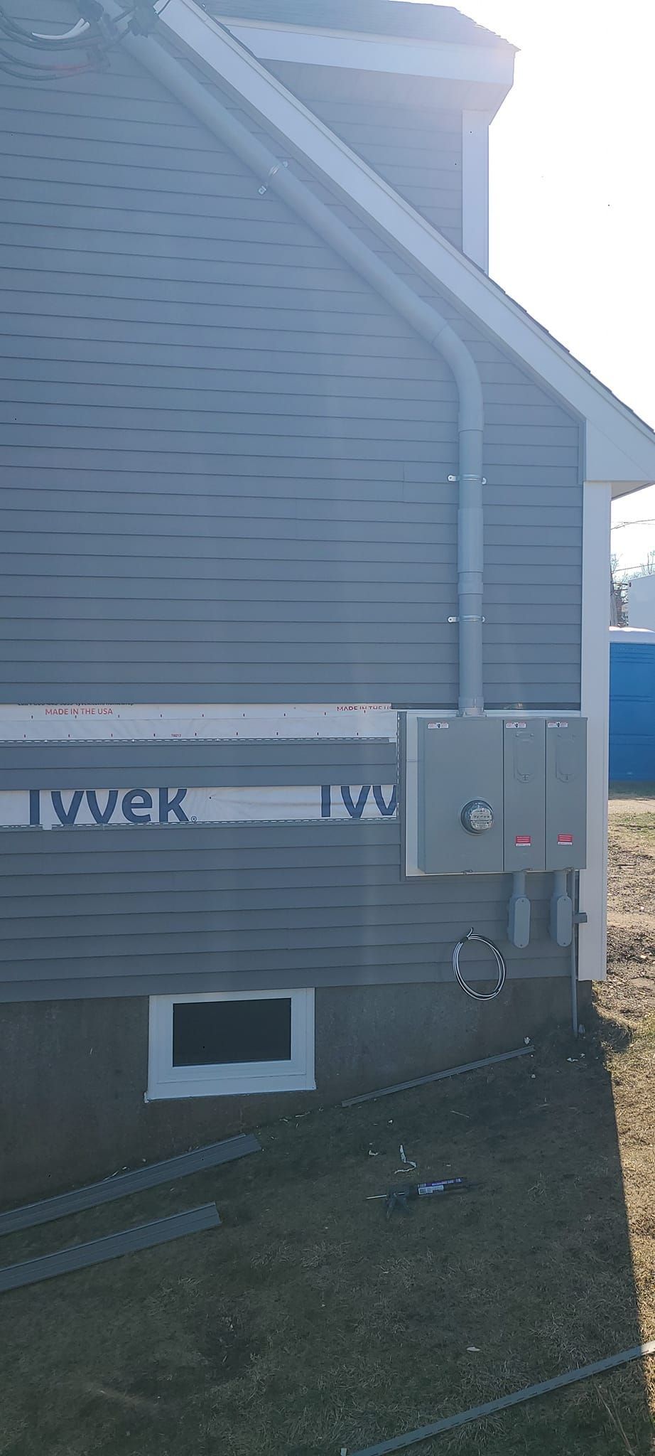 Side view of a gray house exterior with utility meter boxes and a small window near the ground.