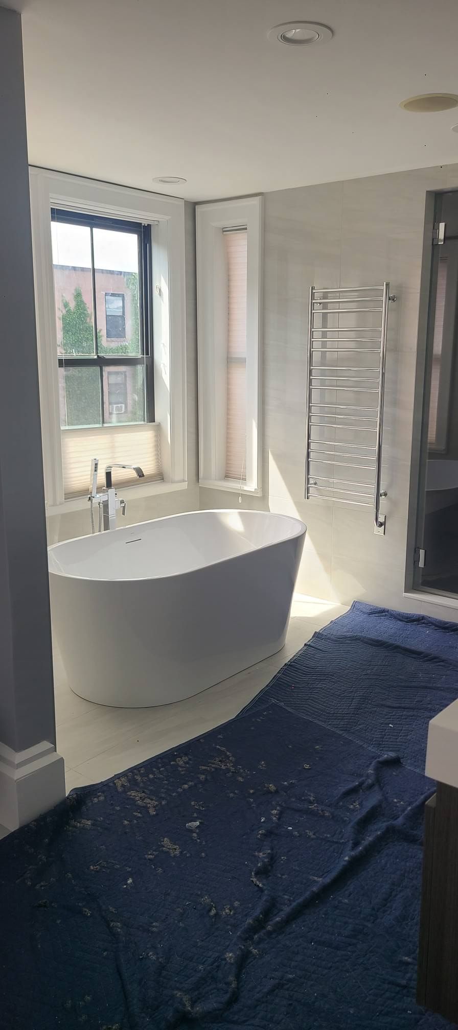 Modern bathroom with a freestanding tub, window, towel rack, and blue floor covering