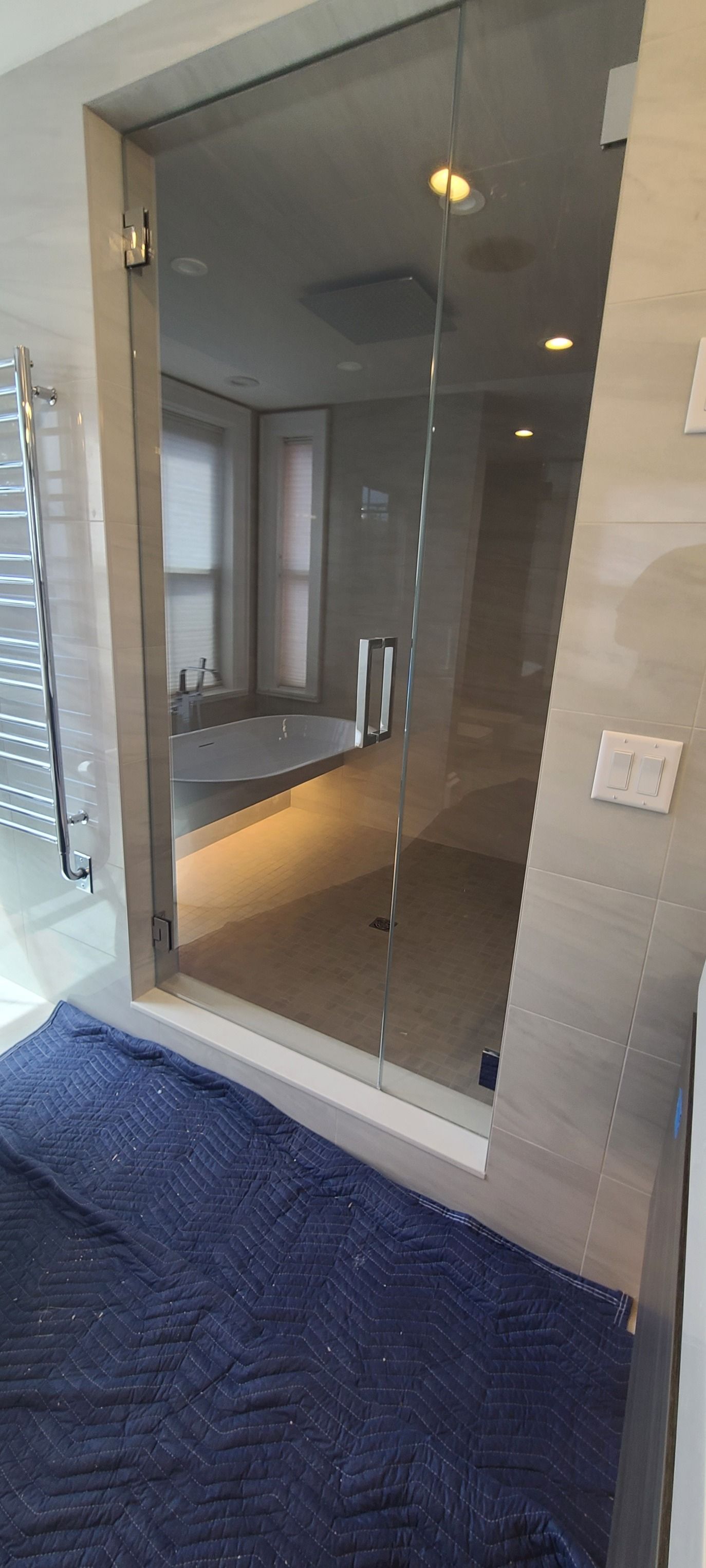 Glass shower enclosure with black trim in a tiled bathroom, viewed from the doorway