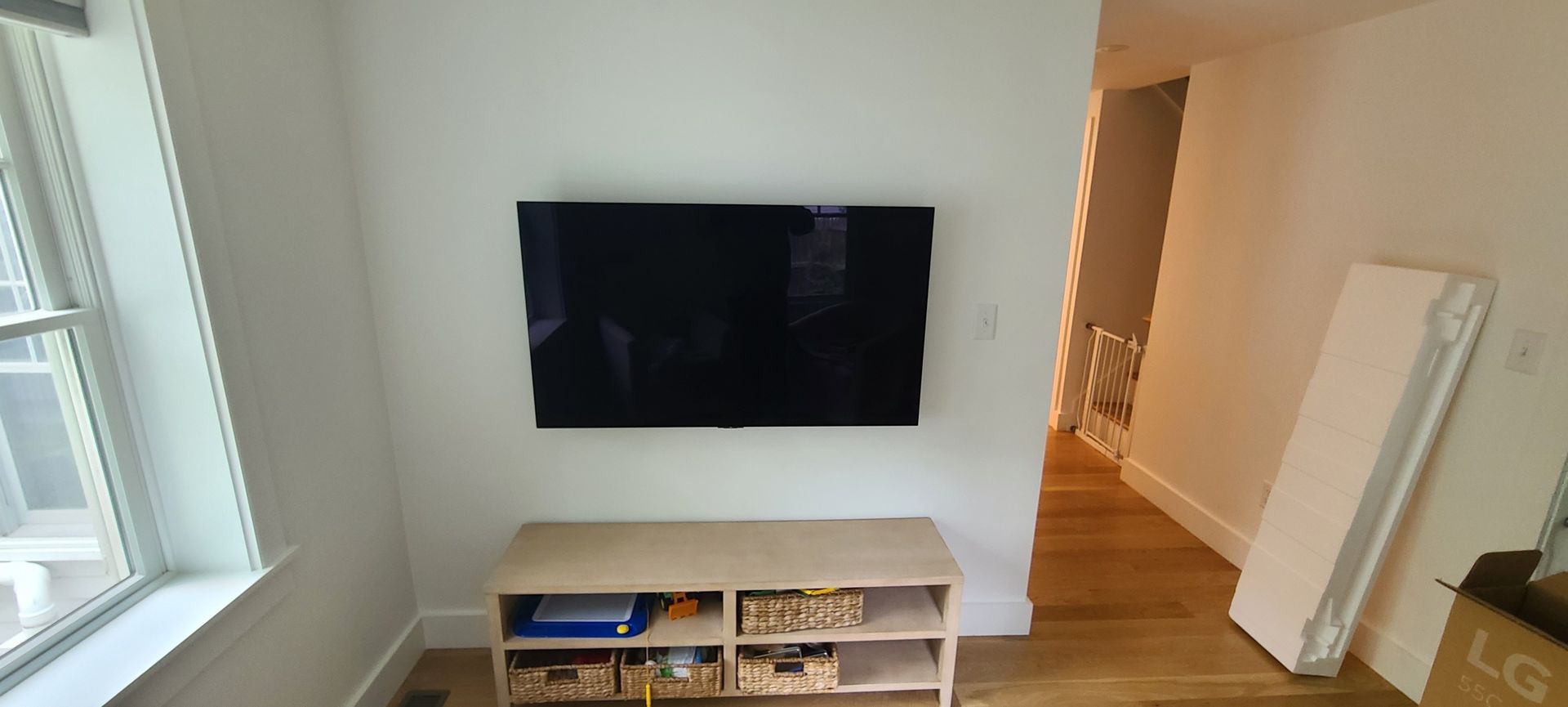 Minimal living room with wall-mounted TV, white media console, and a bright window on the left.