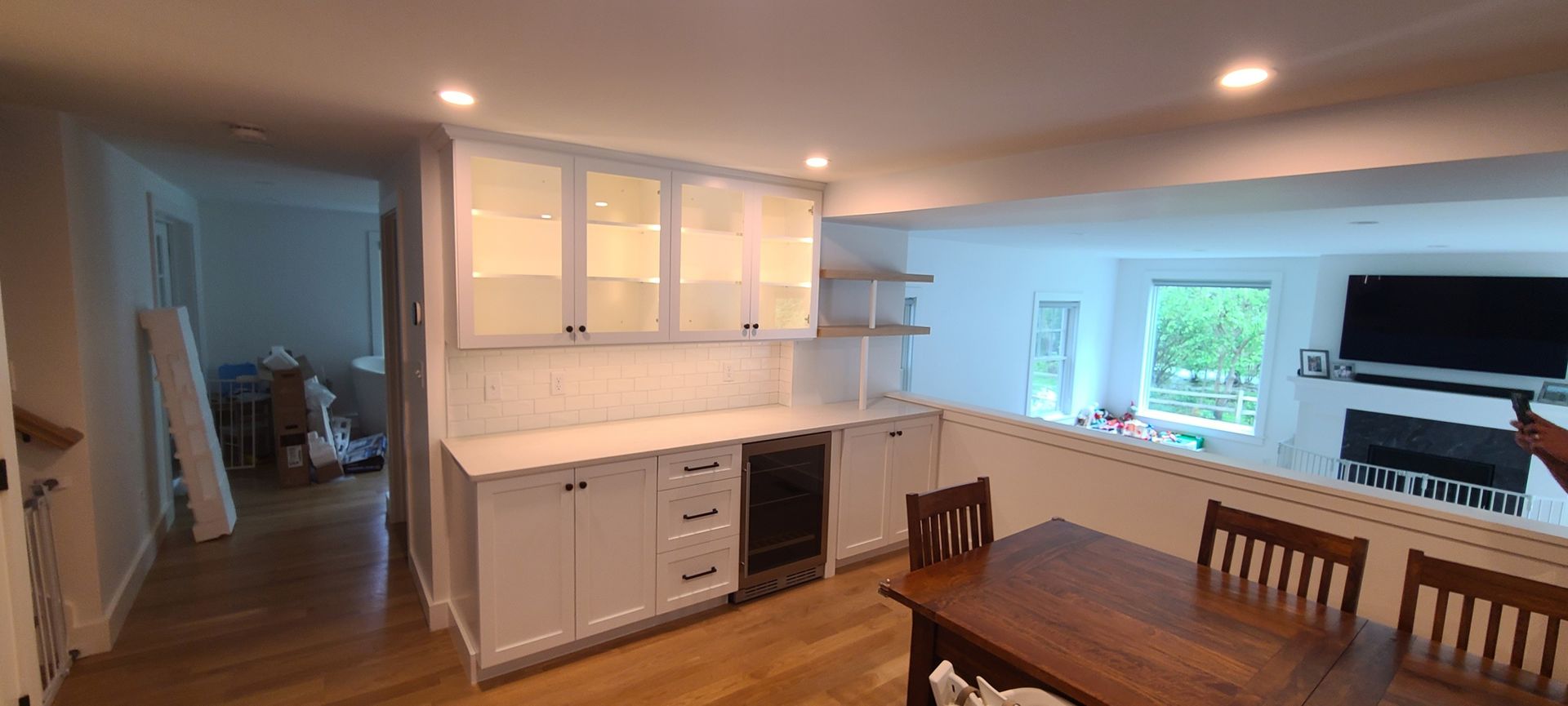 Bright open kitchen and dining area with white cabinets, wooden table, and large windows.