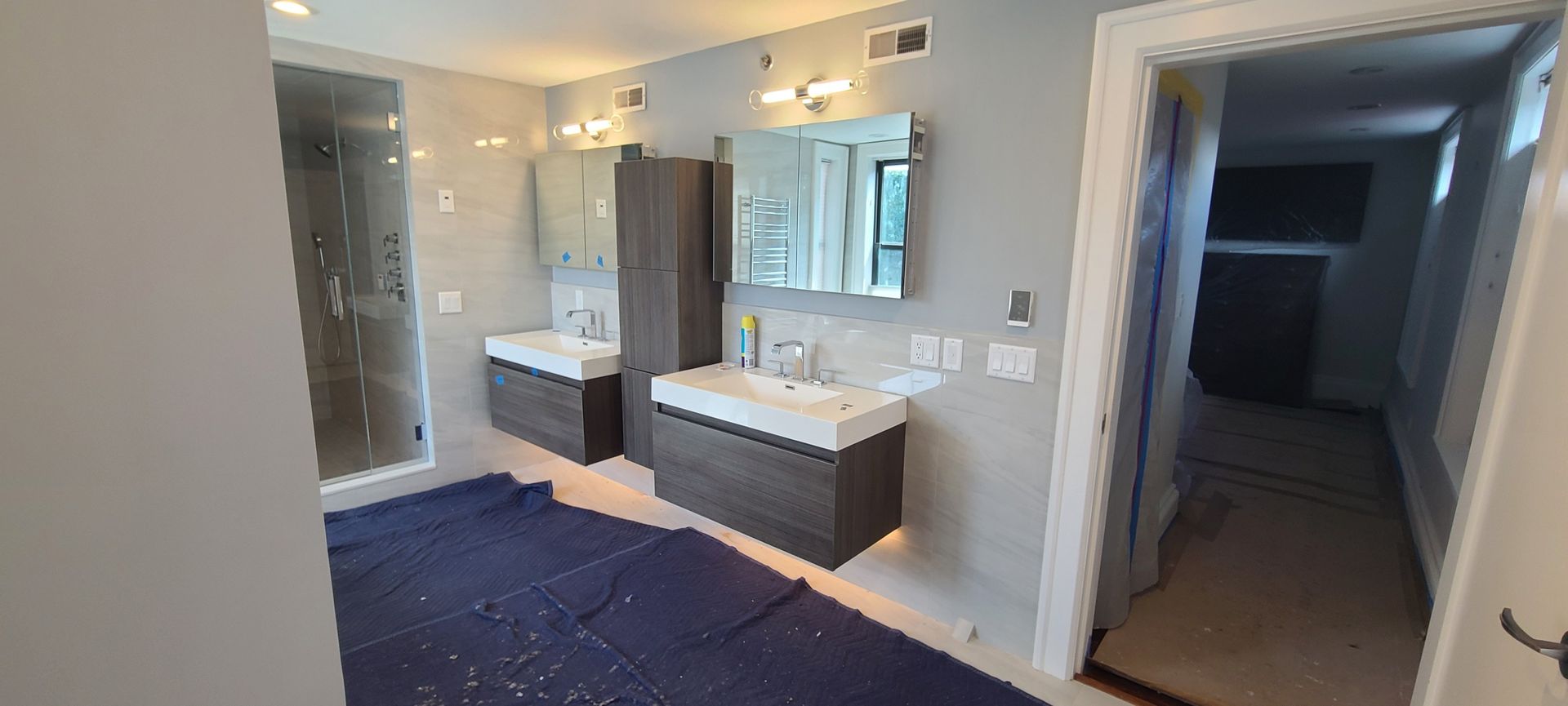 Modern bathroom with double vanity, glass shower, and dark hallway beyond the doorway