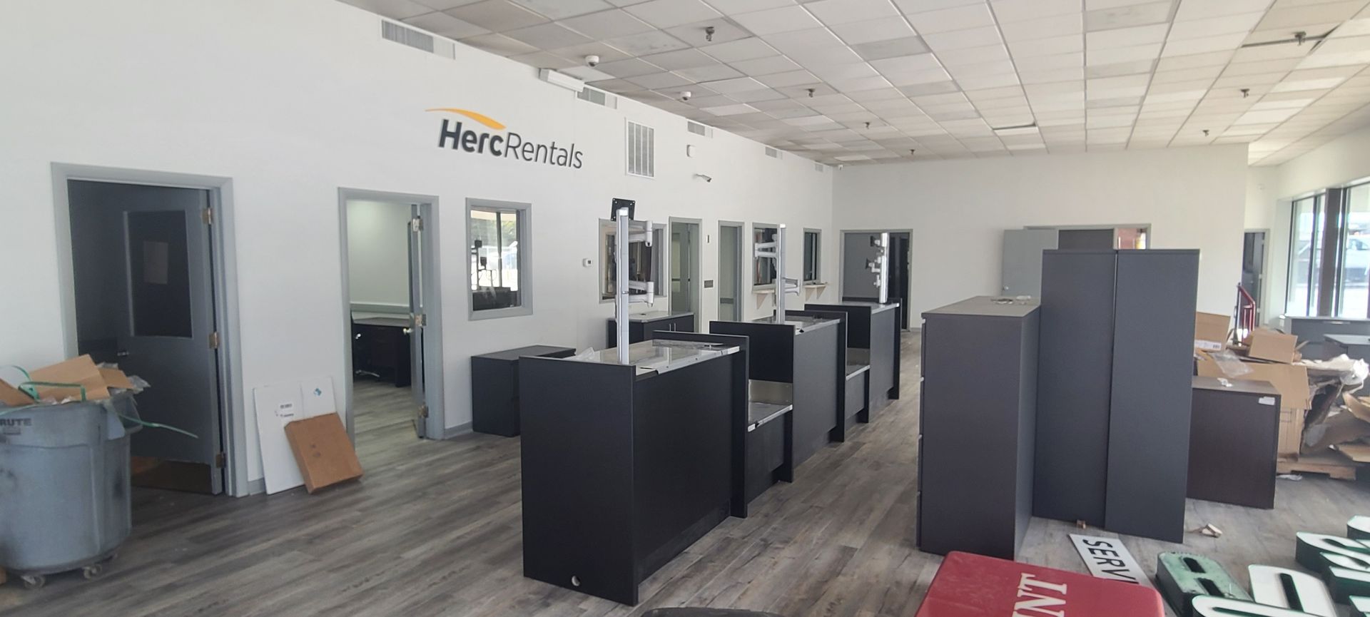 Empty office showroom with cubicles, black desks, and gray carpet under bright ceiling lights