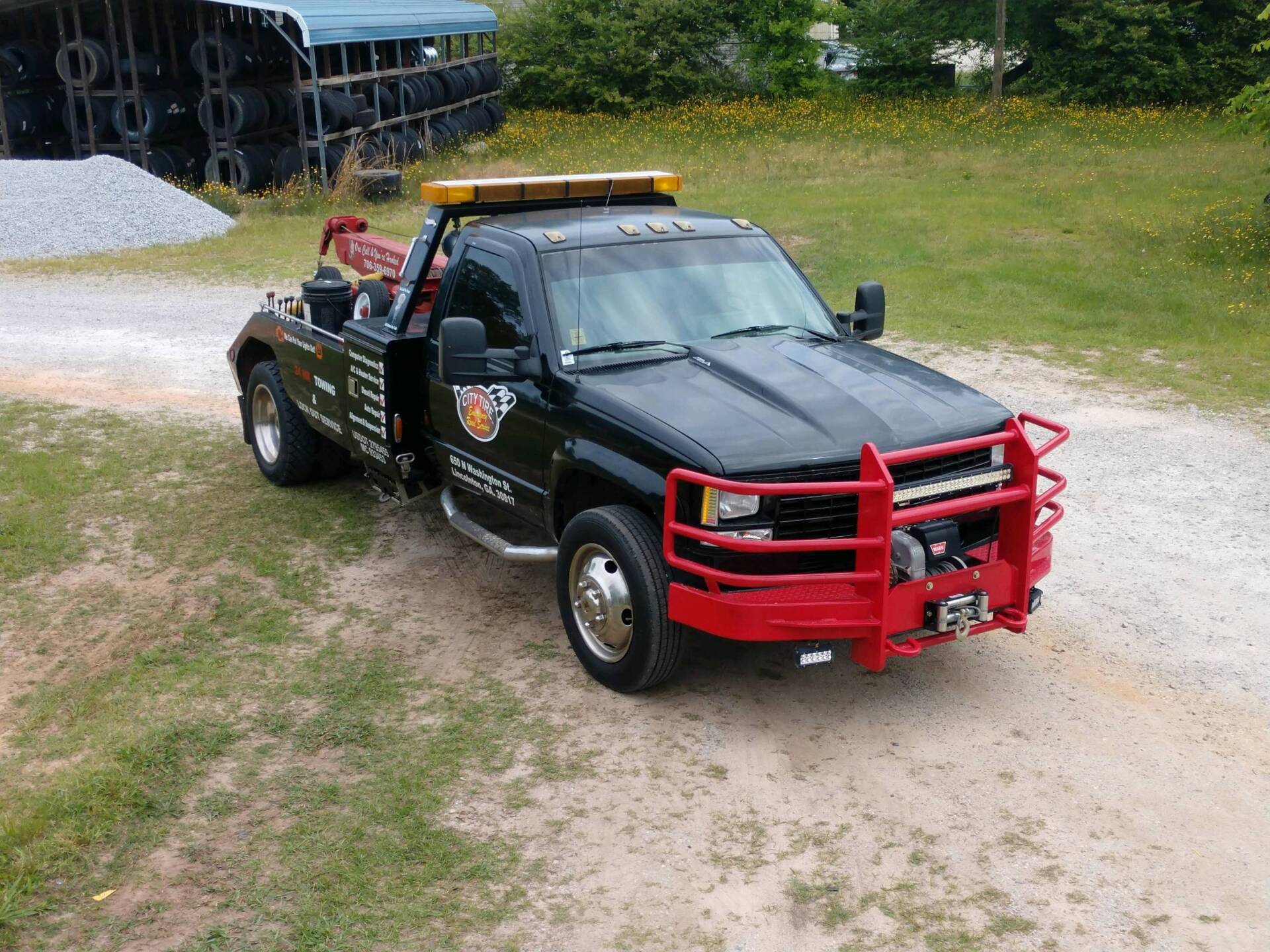 Black tow truck with red accents parked on gravel and grass.