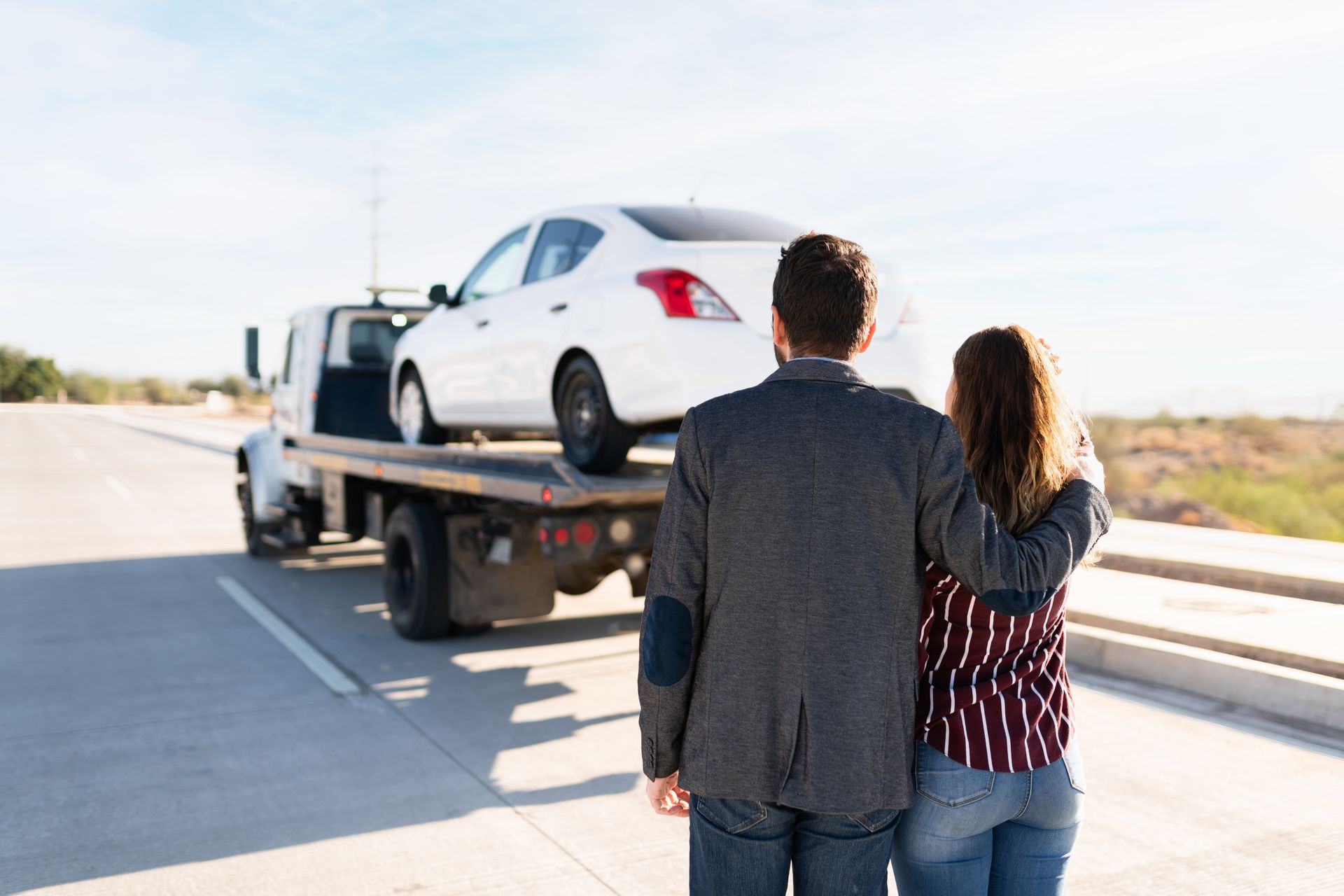 A tow truck loading a stranded car while two people look on. A tow truck loading a stranded car while two people look on.